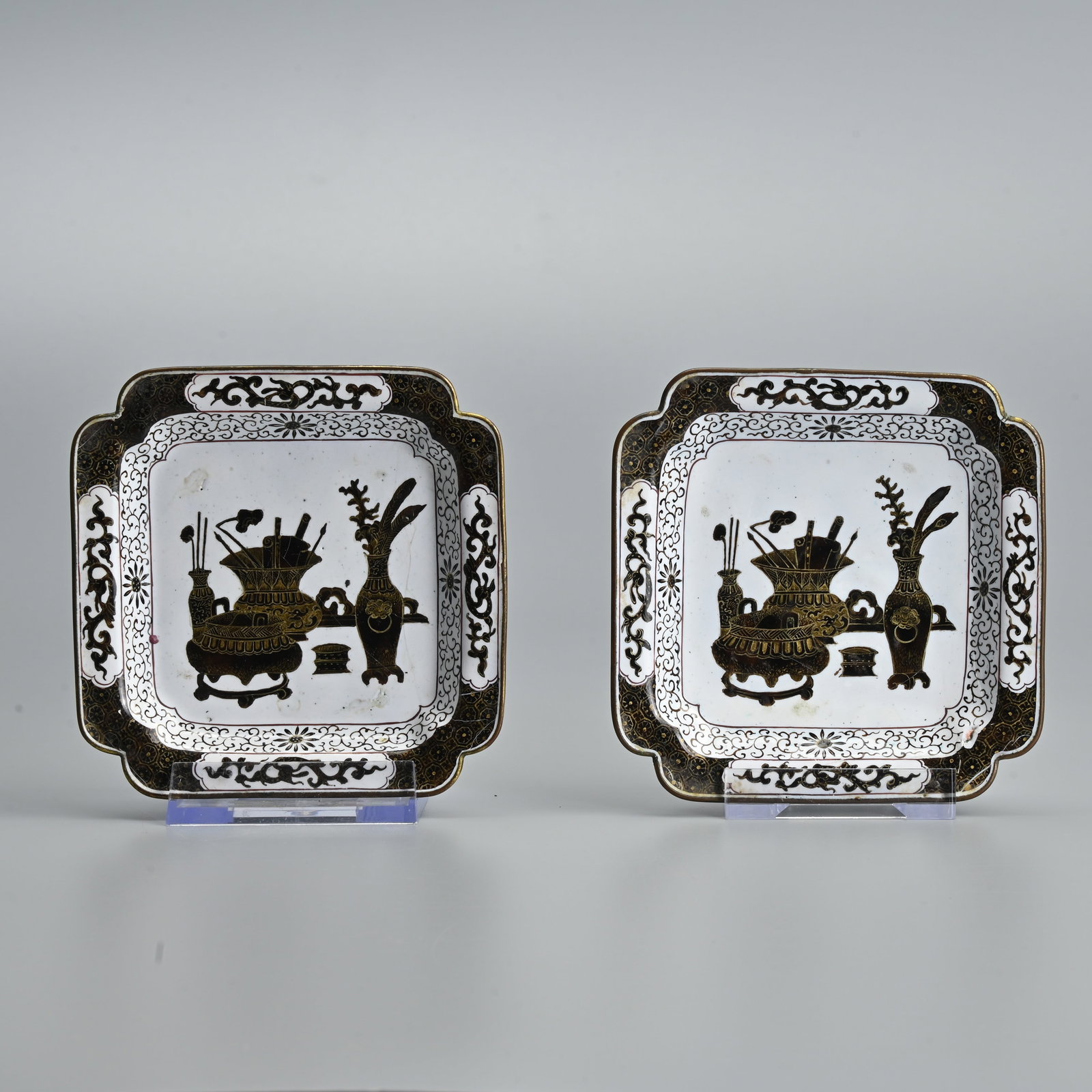 A PAIR OF CHINESE CANTON ENAMEL SQUARE FORM DISHES, QING DYNASTY.: A matching pair, finely decorated with scholar's objects in black and white enamel with gilt detailing. The exterior with fruit sprays and central stylised chilong roundel. 10.4cm wide. (2).