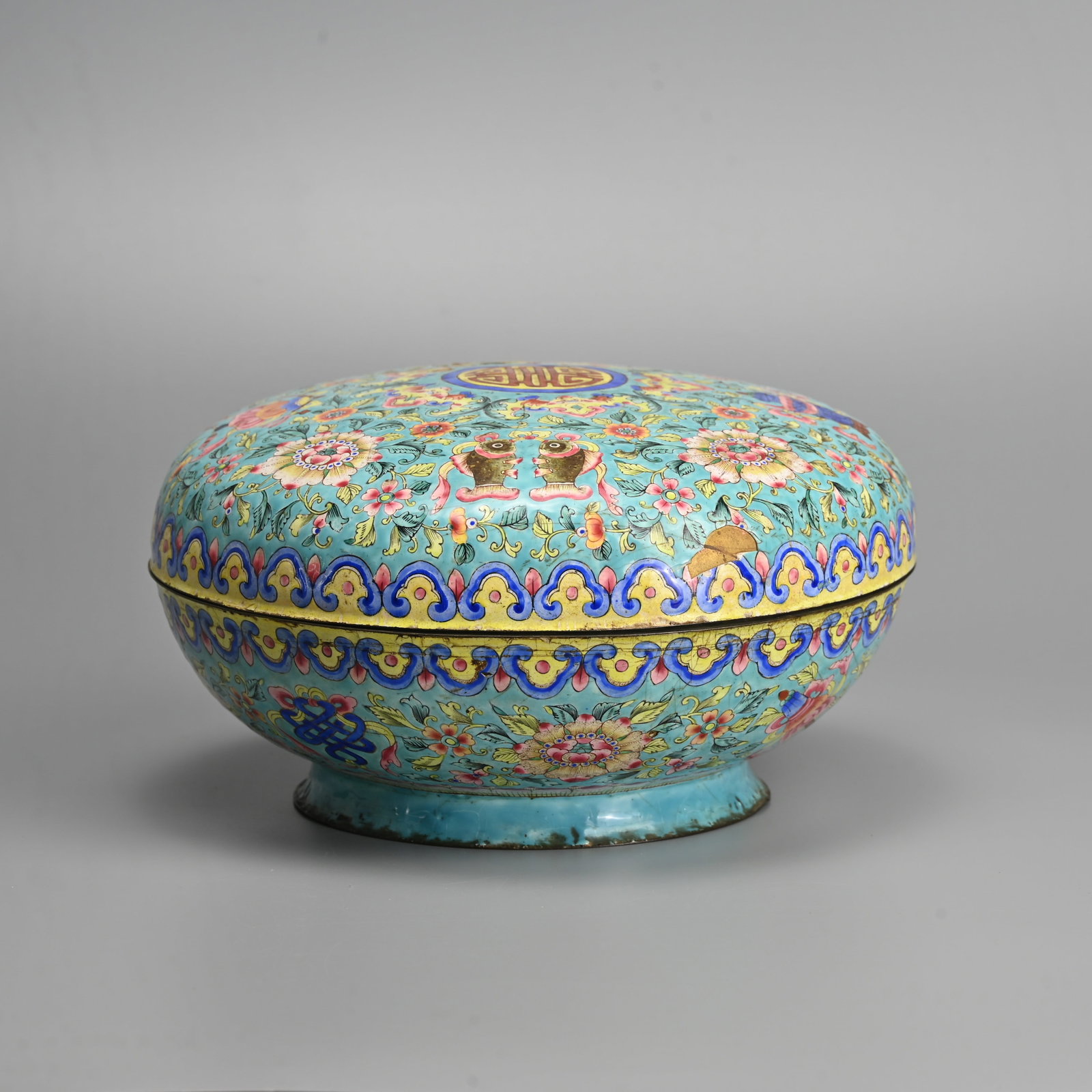 A LARGE CHINESE CANTON ENAMEL BOX AND COVER, QING DYNASTY, 18/19TH CENTURY.: Of circular form densely decorated with Buddhist emblems and various floral spays between rows of bats, ruyi heads an lotus lappets with 'Shou' medallion to the cover. Reserved on a turquoise ground, 