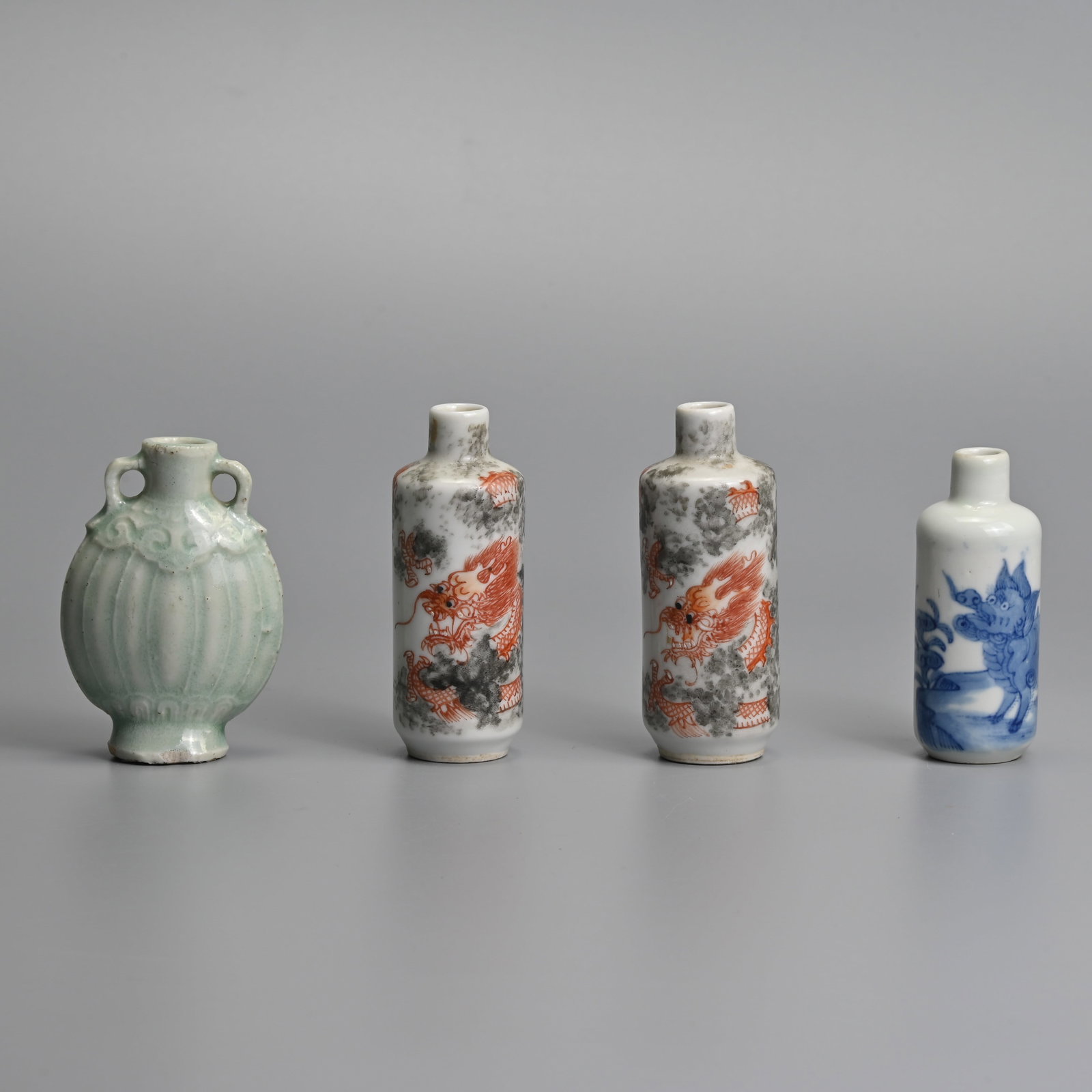 A GROUP OF FOUR CHINESE PORCELAIN SNUFF BOTTLES, 19/20TH CENTURY.: To include a close pair of cylindrical bottles decorated in iron red with dragons emerging from clouds; A blue and white cylindrical bottle featuring a Buddhistic lion; Together with a flattened ovoid