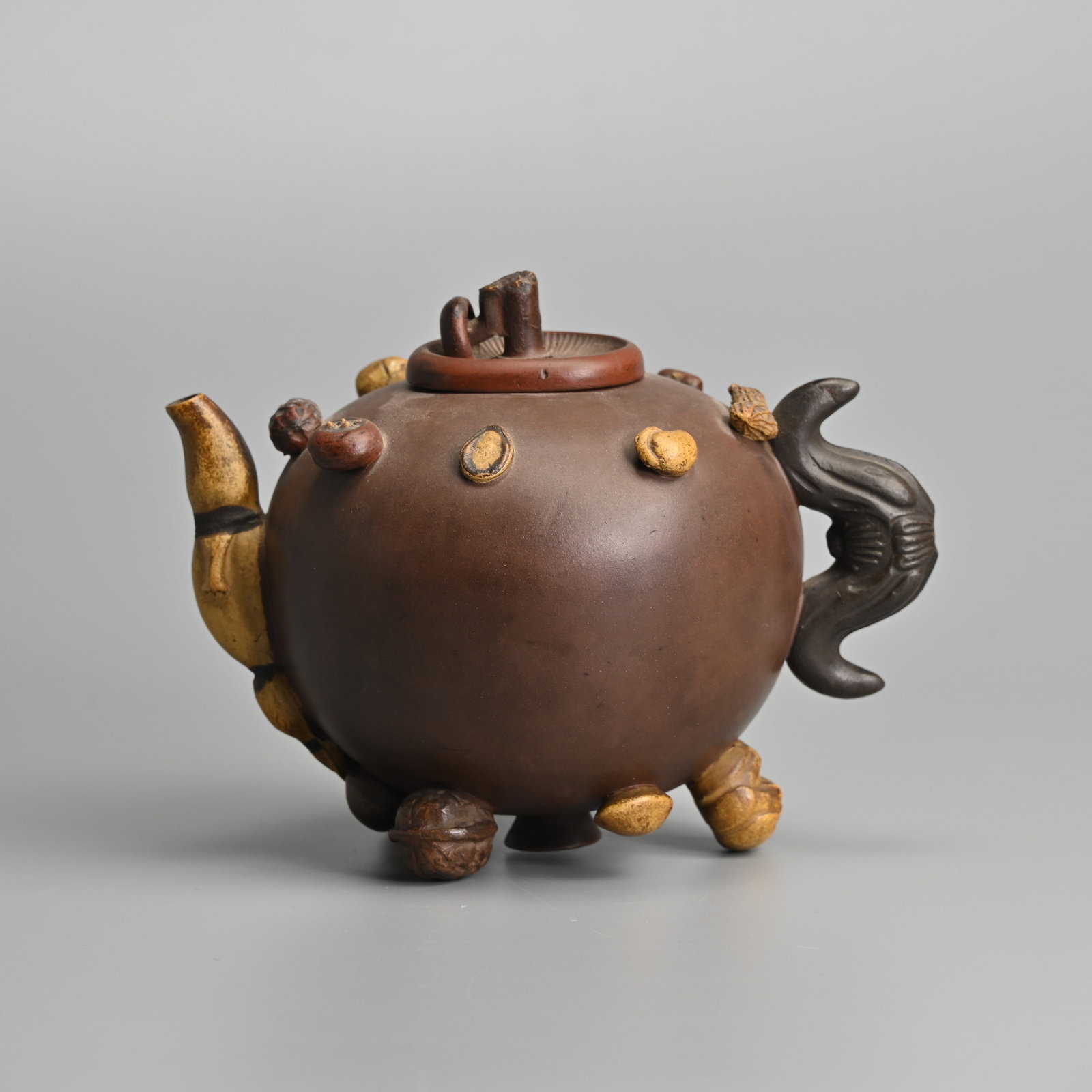 A RARE CHINESE YIXING STONEWARE 'HUNDRED FRUIT' TEA POT AND COVER, LATE QING DYNASTY, 19/20TH: Applied with various fruit and nuts with a mushroom form cover, bat handle and gourd spout. One of the feet in he form of a lotus pod has separate potted 'seed's which are loose in the pod. The cover 