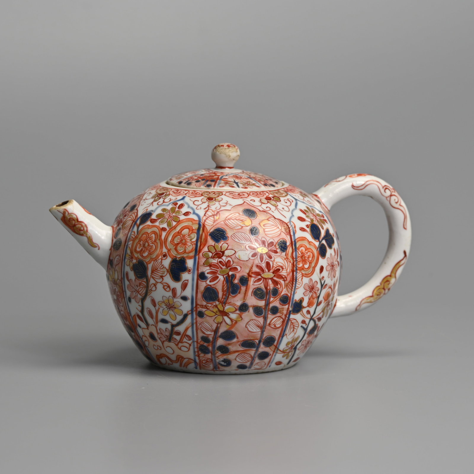 A CHINESE PORCELAIN IMARI GLOBULAR TEAPOT AND COVER, EARLY 18TH CENTURY, KANGXI.: Painted with lappet-shaped panels of chrysanthemum and other flowers and leaves, with clouds and scrolls to the handle and spout, 10.5 cm high.