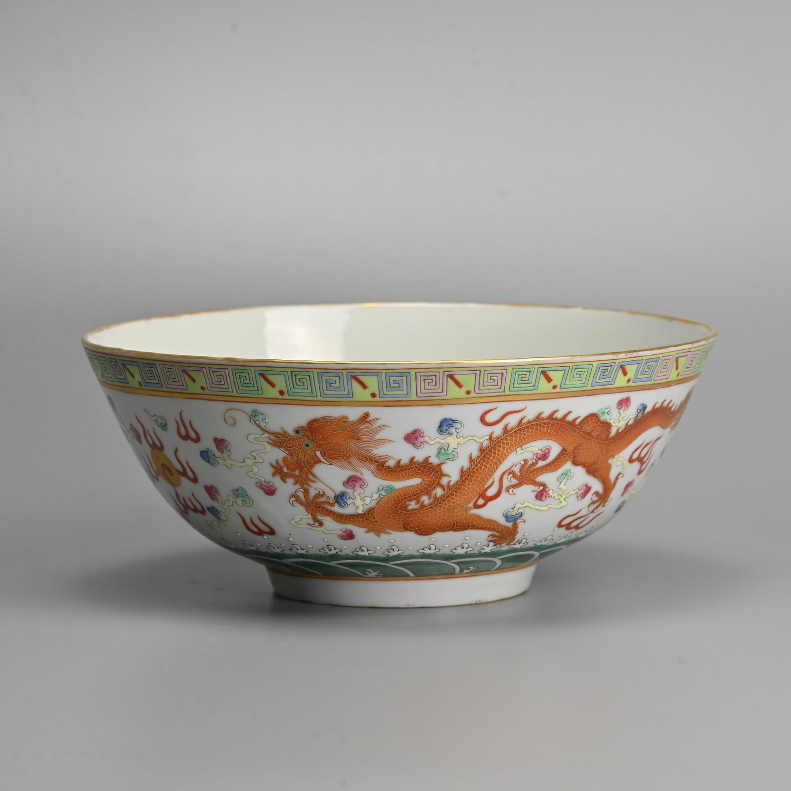 A LARGE CHINESE FAMILLE ROSE PORCELAIN 'DRAGON AND PHOENIX' BOWL, GUANGXU MARK.: Featuring dragon and phoenix in flight amidst ruyi clouds and flames above crashing waves below a band of key fret to the rim on a lime green ground and gilt rim. Six character mark of Guangxu to base