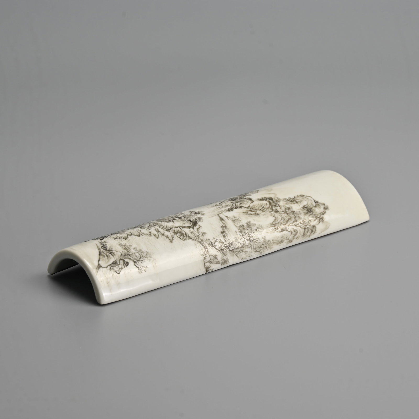 A CHINESE GRISAILLE DECORATED PORCELAIN WRIST REST, QING / REPUBLIC PERIOD.: Decorated with mountainous landscape scene with buildings and figures crossing bridge. 20.4cm length.