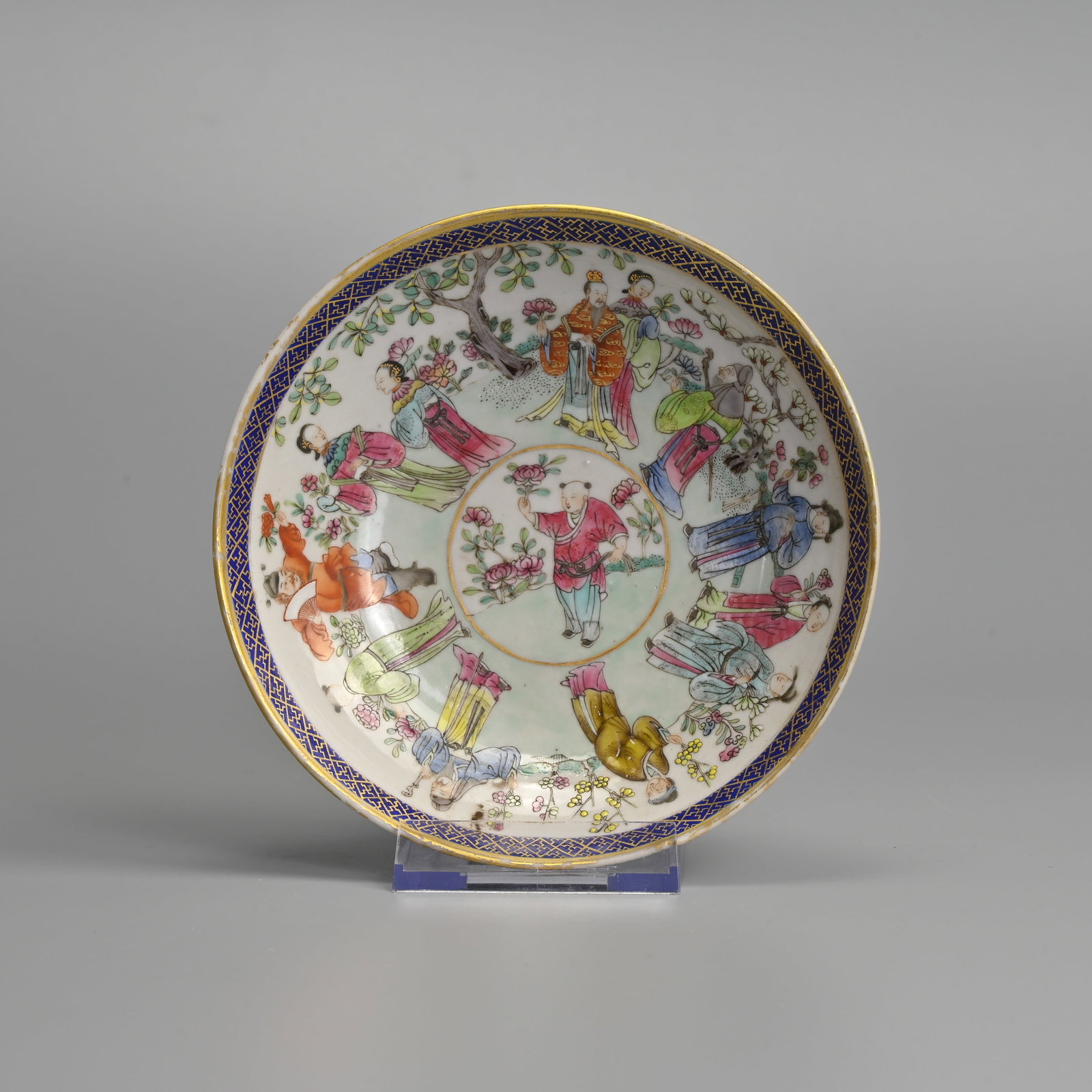 A CHINESE FAMILLE ROSE PORCELAIN DISH, JIAYIN TANG ZHI MARK.: Decorated with various figures in a garden scene holding floral sprays. The central roundel with a boy holding a peony. Within a wanzi pattern border in gilt on a deep blue ground. The base with four 