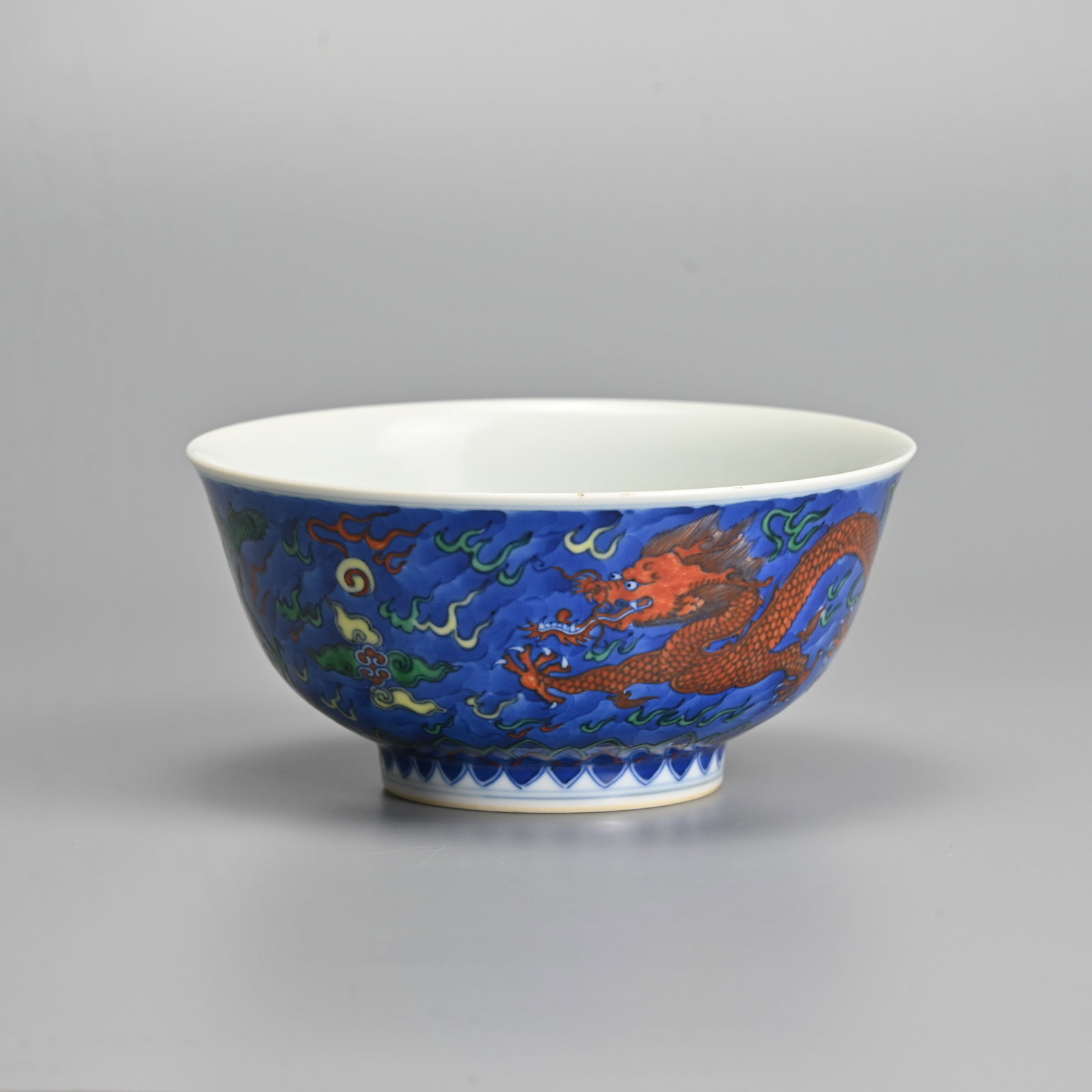 A CHINESE GREEN, YELLOW AND IRON RED DECORATED AND UNDERGLAZE BLUE GROUND PORCELAIN 'DRAGON' BOWL,: Featuring two dragons chasing flaming pearls amidst cloud scrolls and flames. A third green glazed dragon medallion to the interior. Six character mark of Kangxi to base in underglaze blue. 14cm diam.