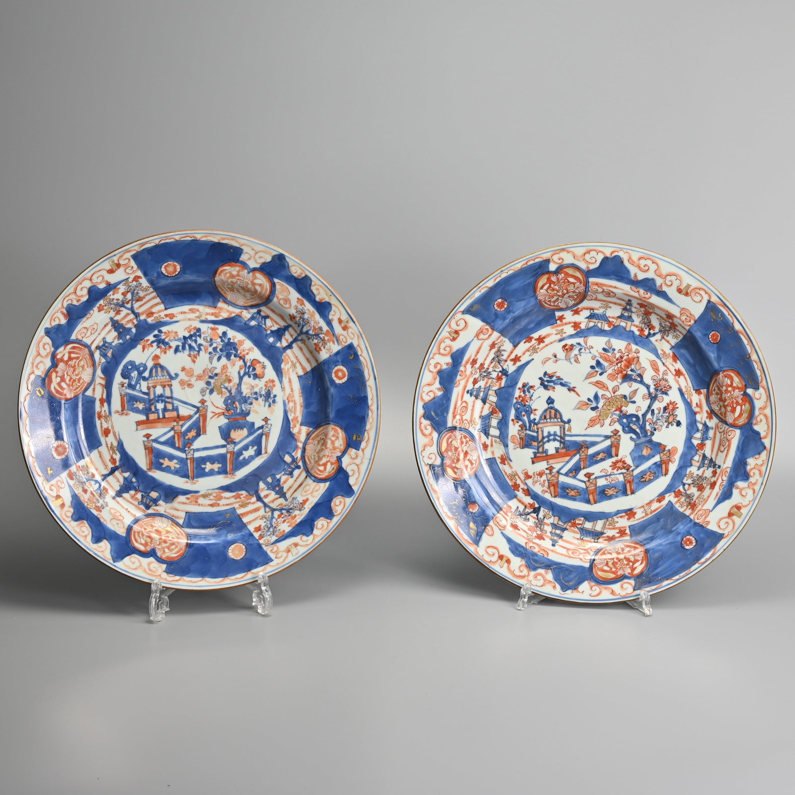 A LARGE PAIR OF CHINESE IMARI PORCELAIN DISHES, KANGXI (1662-1722).: Decorated with a fenced garden featuring a pavilion and jardiniere surround by shaped panels with landscapes and pagodas. Conch shell mark within a double ring in underglaze blue to base. 35cm diam. (