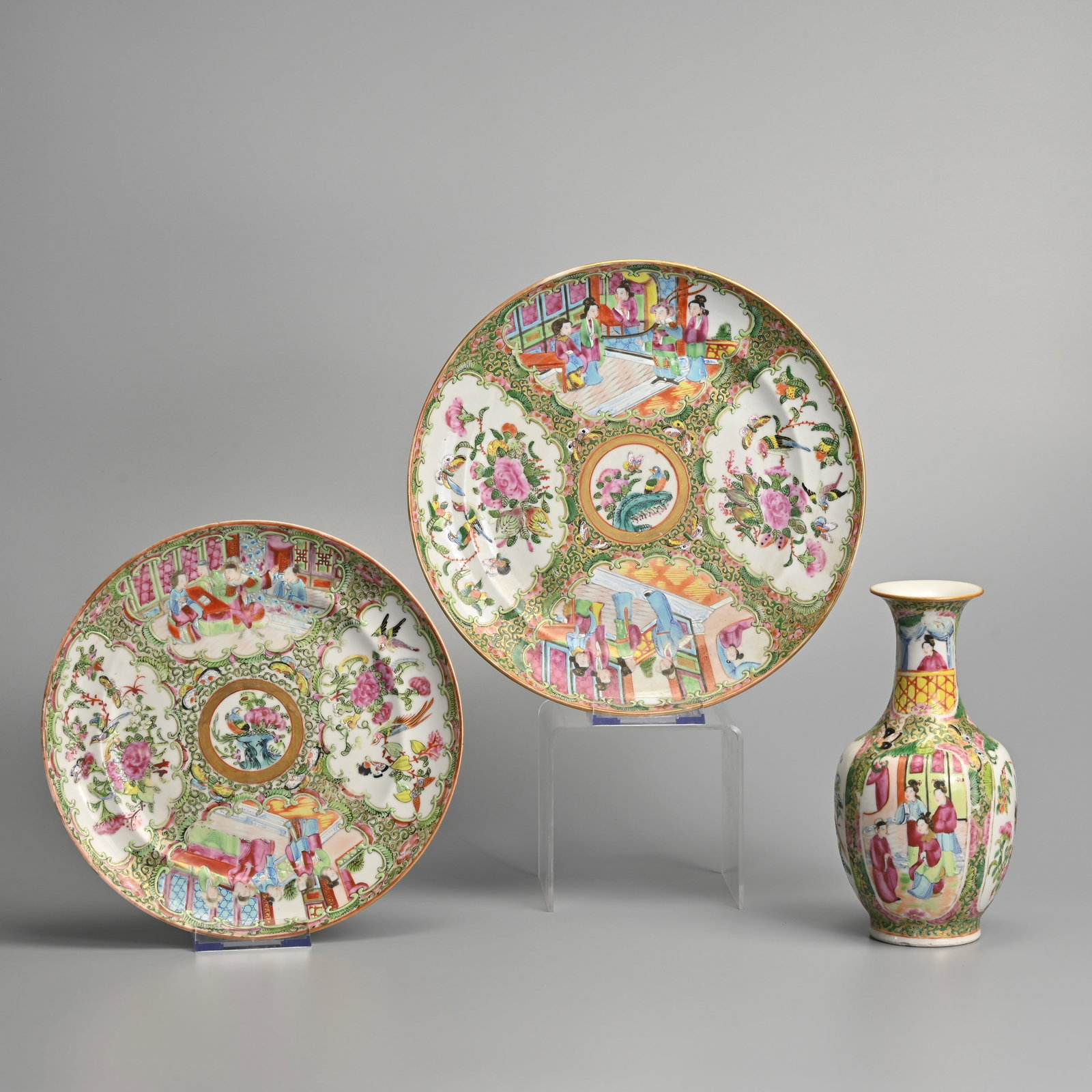 A CHINESE CANTON FAMILLE ROSE PORCELAIN BALUSTER VASE AND TWO PLATES, 19TH CENTURY.: Each painted with scroll-shaped cartouches with figures of ladies in discussion alternating with butterflies and insects, reserved on a gilt ground with dense flowers and a gilt-ground, the vase 18.5 