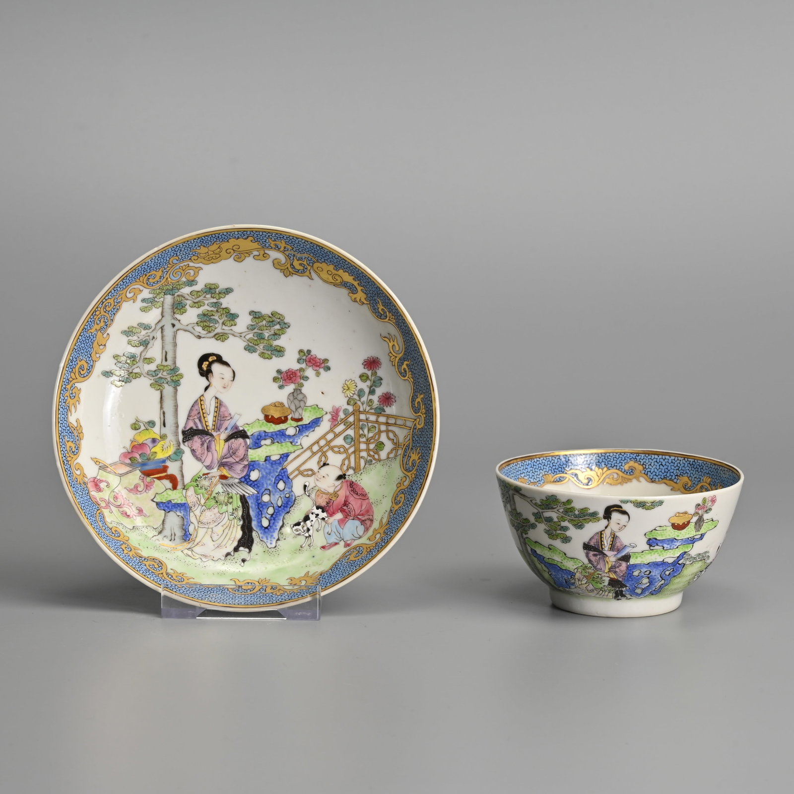 A CHINESE FAMILLE ROSE AND GILT DECORATED PORCELAIN CUP AND SAUCER.: Matching cup and saucer decorated in brightly coloured enamels featuring a lady seated in a garden with a boy playing with a cat. Saucer 13.5cm diam.