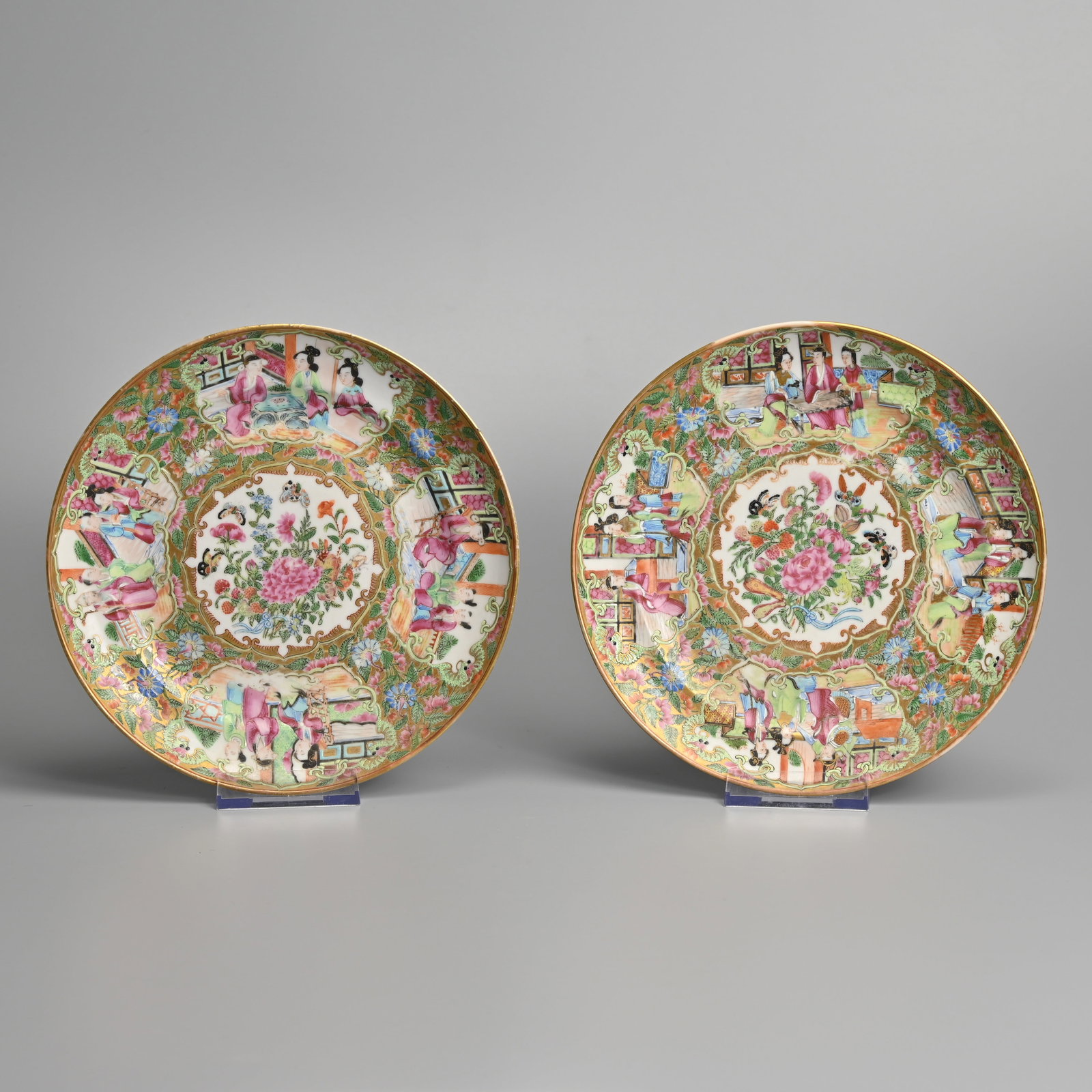 A PAIR OF CHINESE CANTON FAMILLE ROSE PORCELAIN PLATES, 19TH CENTURY.: Each painted with a central bouquet of flowers and scattered butterflies, within borders of scroll-shaped cartouches painted with figures of ladies in discussion, reserved on a ground of dense flowers