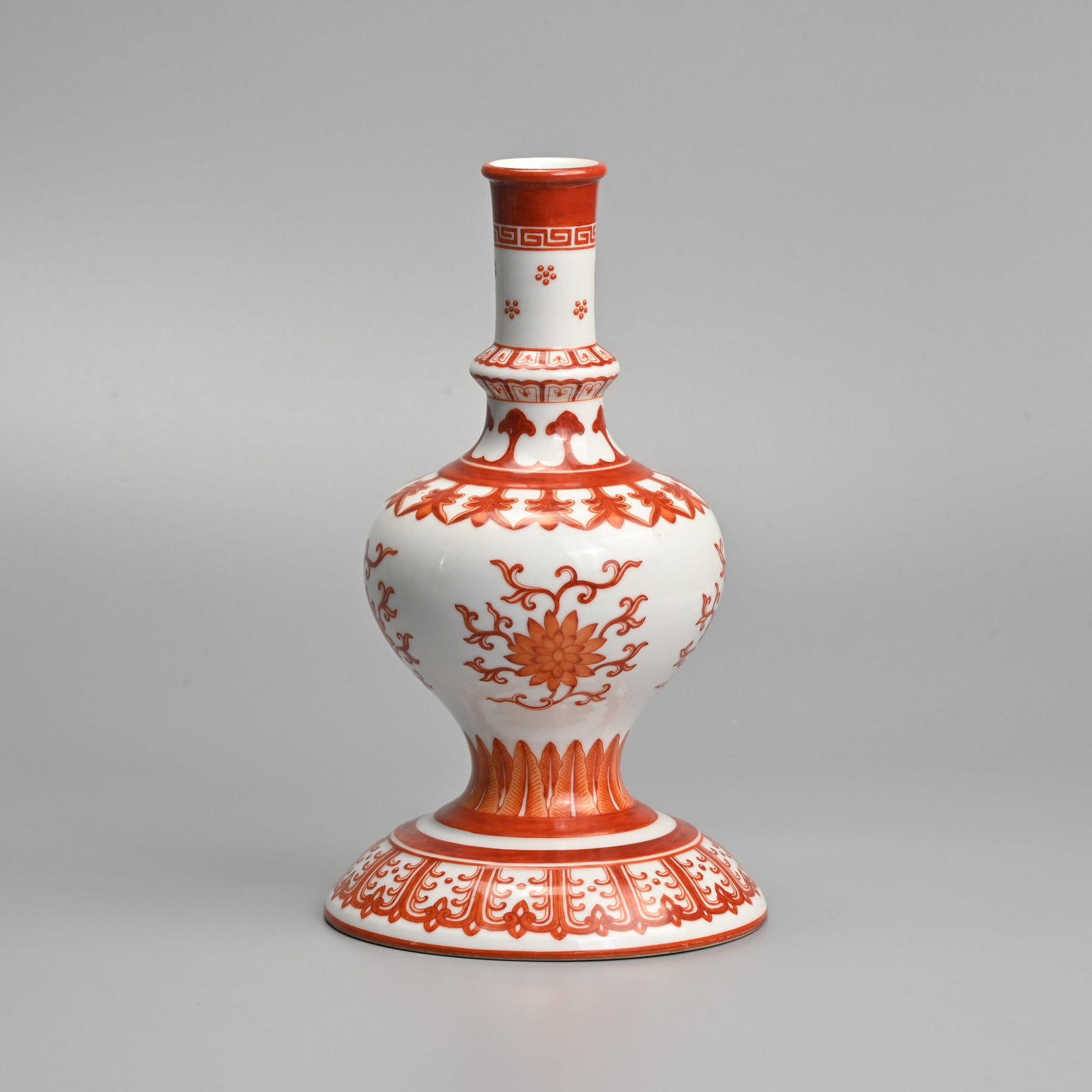 A CHINESE IRON RED DECORATED PORCELAIN 'HOLY WATER' ALTAR VASE, PROBABLY 20TH CENTURY.: Ovoid body on a wide splayed domed base with a tall waisted cylindrical neck, decorated with lotus sprays with various bands of lappets, ruyi heads, key fret and petals all in iron red on a white grou
