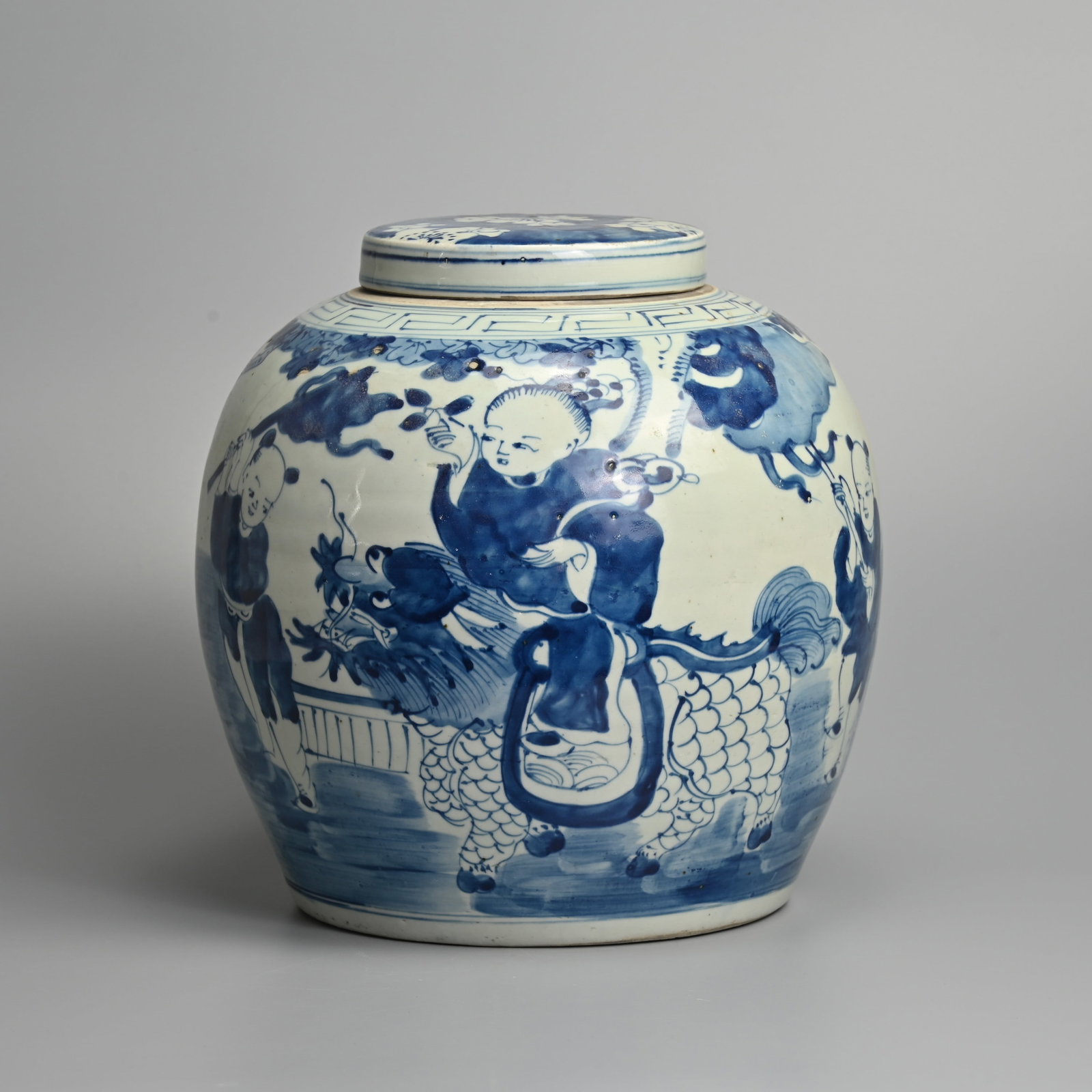 A LARGE CHINESE PORCELAIN BLUE AND WHITE GINGER JAR AND COVER, 20TH CENTURY.: Painted in the Ming style with boys carrying flags before a lion dog in landscape, below Key-pattern border, the reverse with stylised character, 29.5 cm high.