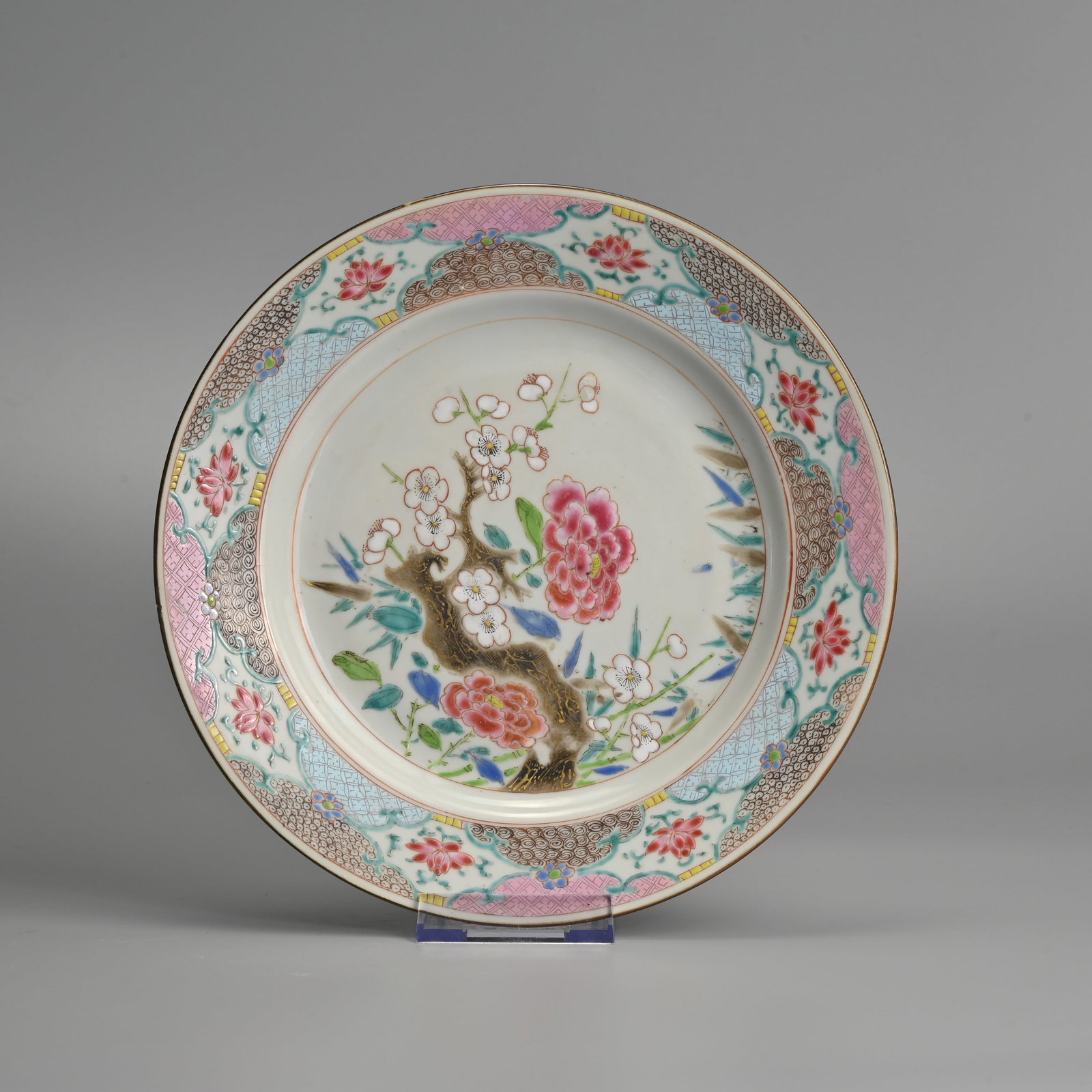 A CHINESE FAMILLE ROSE PORCELAIN DISH, EARLY 18TH CENTURY.: Decorated in brightly coloured enamels with gilding, features a flowering prunus branch and peony blossoms. The border is finely decorated with geometric patterns and flower sprays. 22.5cm diam.