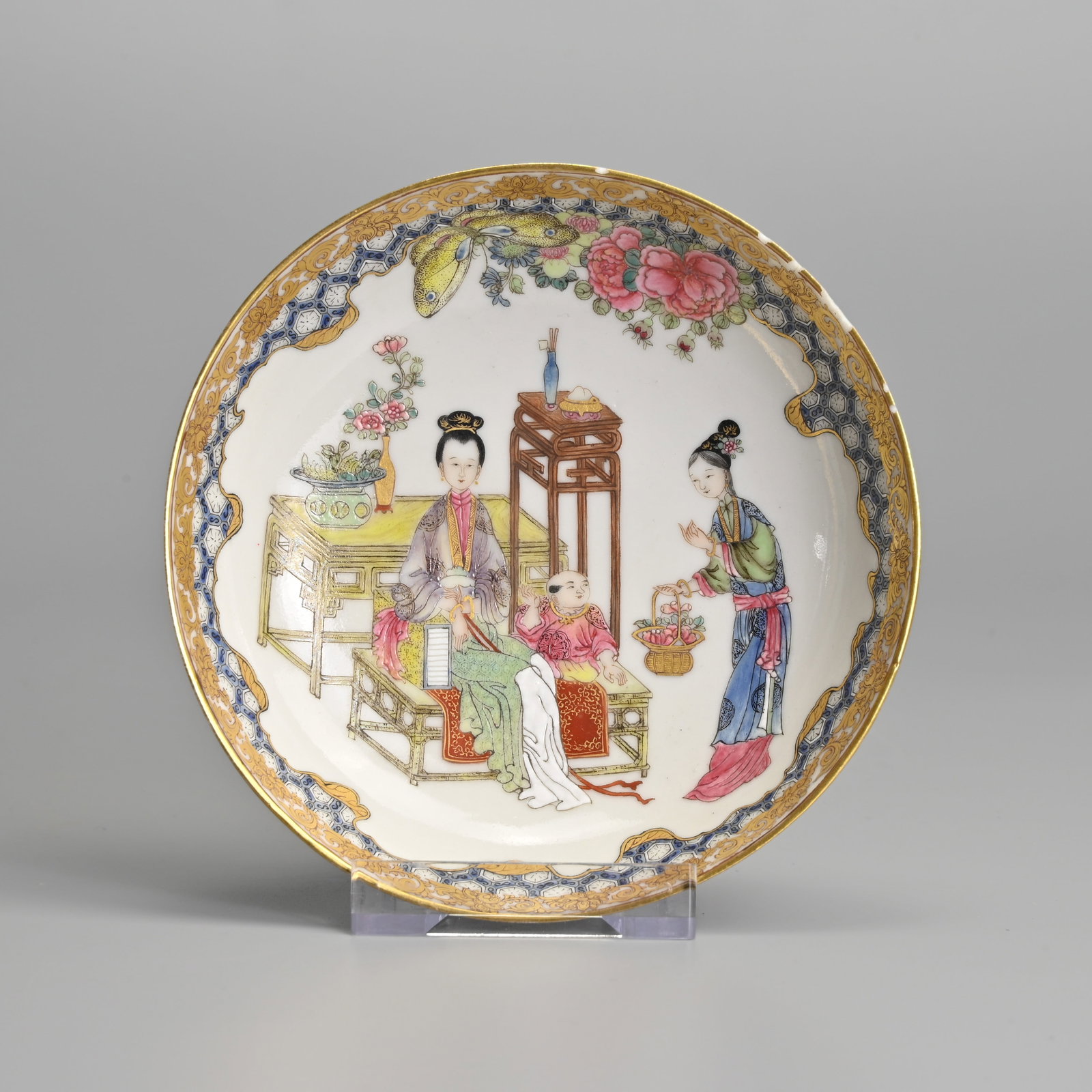 A CHINESE FAMILLE ROSE AND GILT DECORATED PORCELAIN SAUCER.: Decorated with ladies and child beside furniture below a butterfly and peony bloom, within a diaper pattern border with gilt lotus scrolls. 12cm diam.