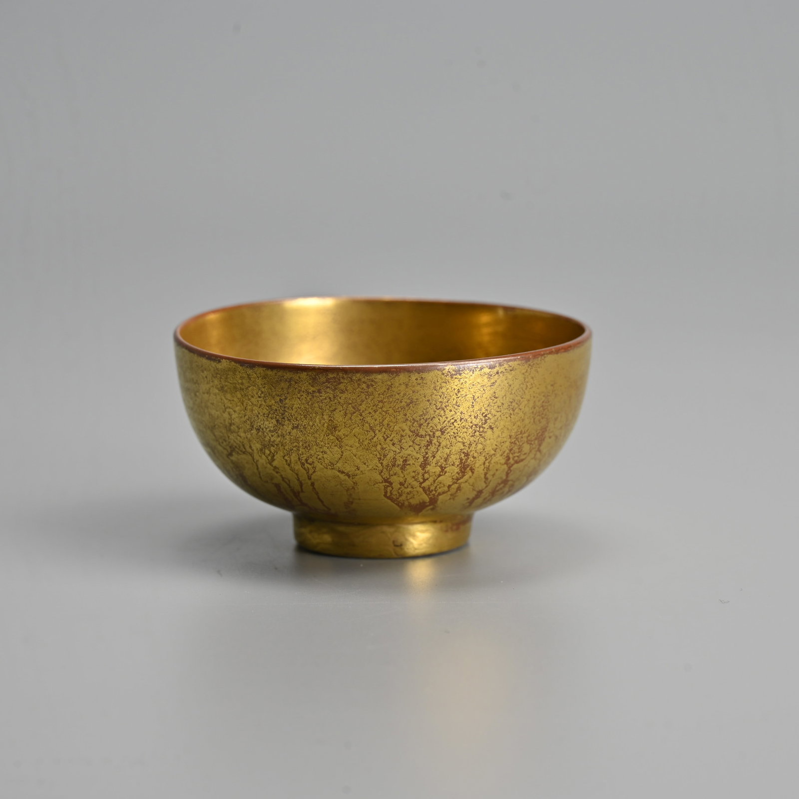A CHINESE GILT DECORATED PORCELAIN WINE CUP, KANGXI MARK.: Rounded body covered in a copper coloured glaze with gilt overlay. Six character mark of Kangxi to base in underglaze blue within a circle. 6.8cm diam.