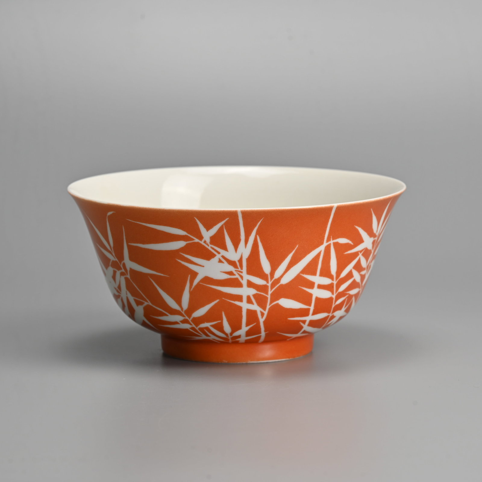 A CHINESE CORAL GROUND REVERSE DECORATED PORCELAIN 'BAMBOO' BOWL, GUANGXU MARK, 20TH CENTURY.: Rounded body with gently everted rim decorated with leafy bamboo canes rising from the foot. Six character mark of Guangxu to base. 16.5cm diam.