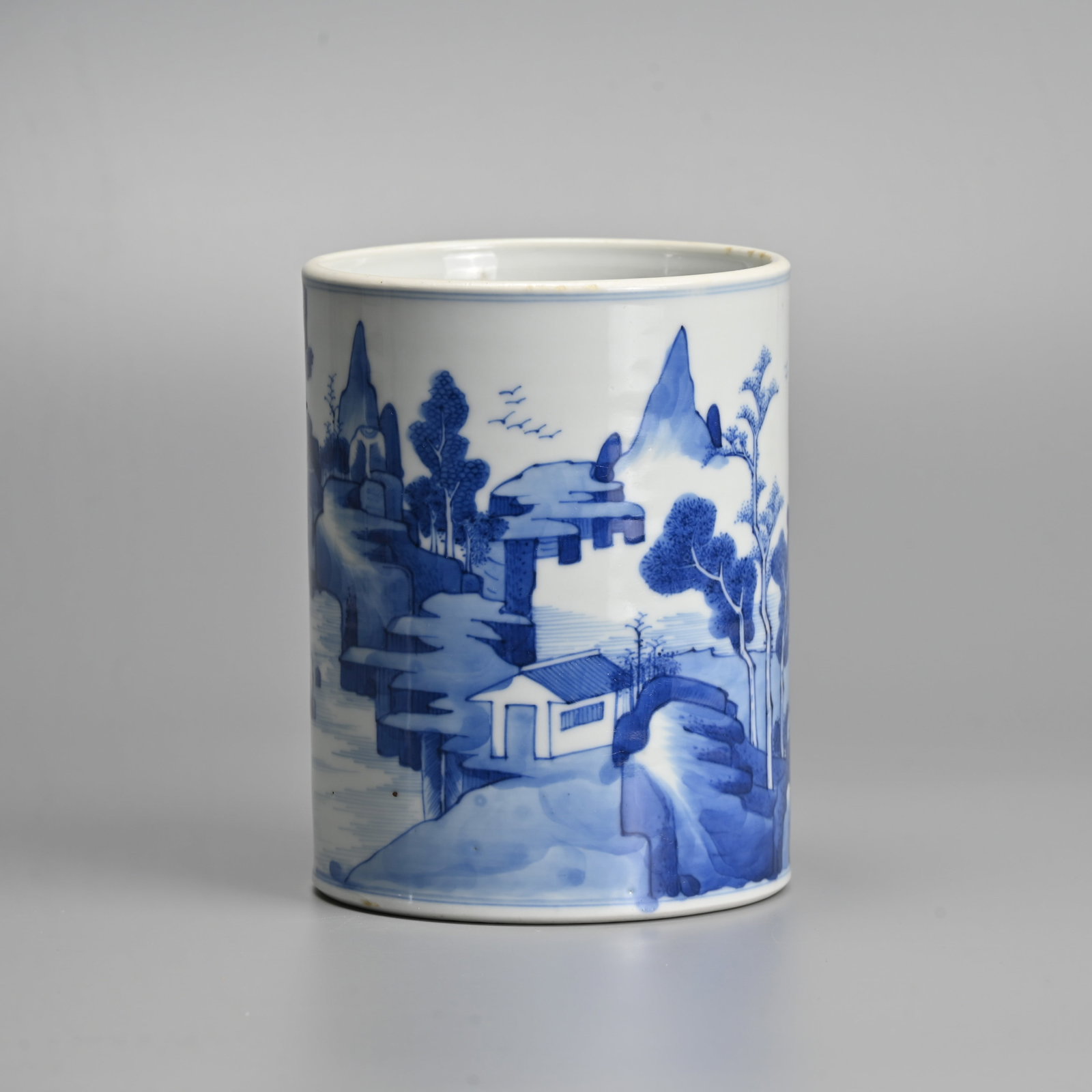 A CHINESE BLUE AND WHITE PORCELAIN BRUSH POT, BITONG, 20TH CENTURY.: Heavily potted, decorated with a landscape scene featuring scholars seated playing weiqi before a rocky landscape with buildings and river with sampan. 15cm tall x 11.5cm diam.