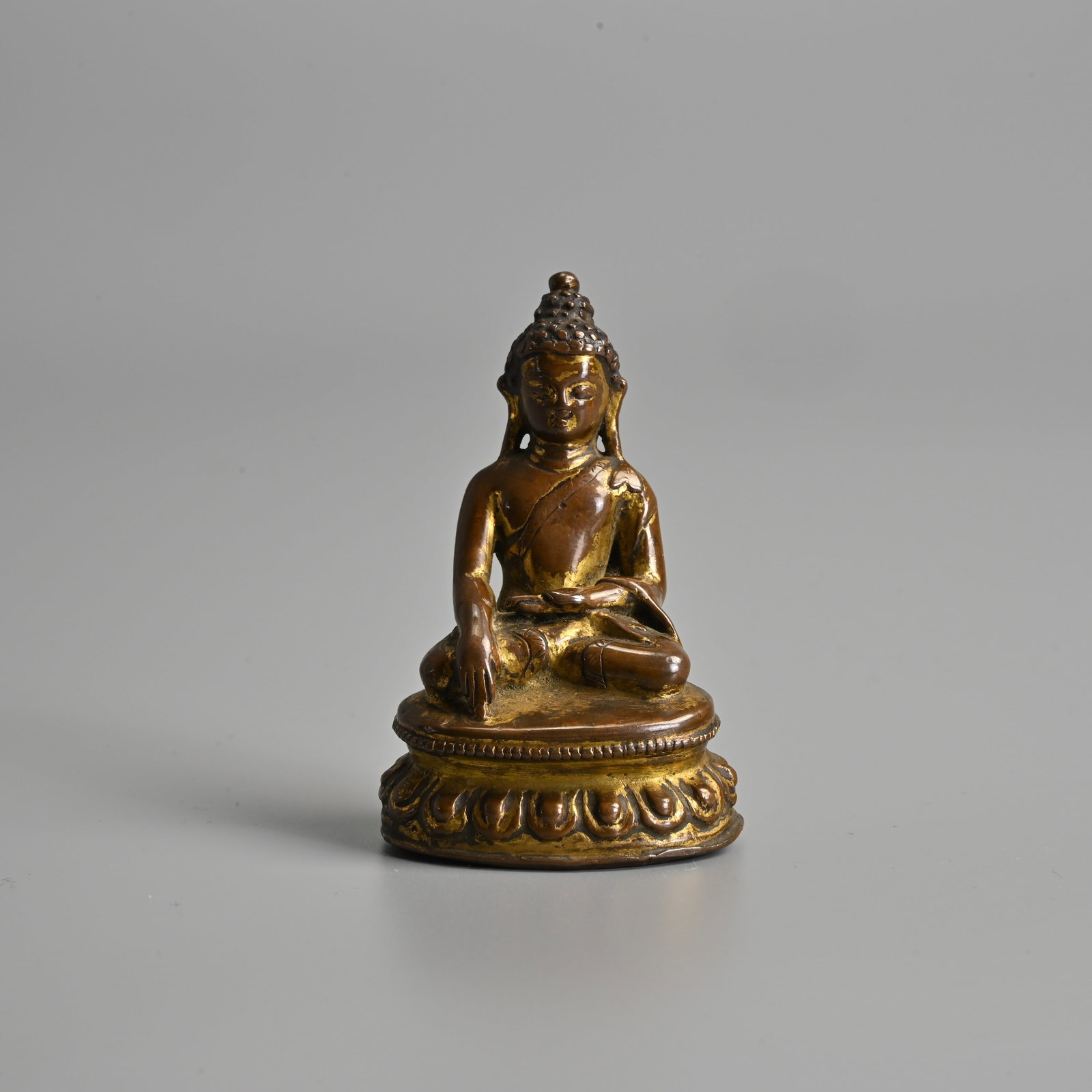 A SMALL TIBETAN GILT COPPER ALLOY FIGURE OF BUDDHA, 17TH CENTURY OR EARLIER.: Figure of Shakyamuni seated in meditation on a lotus base wearing a dhoti draping over the left shoulder. 6.2cm tall. Weight 92 grams.