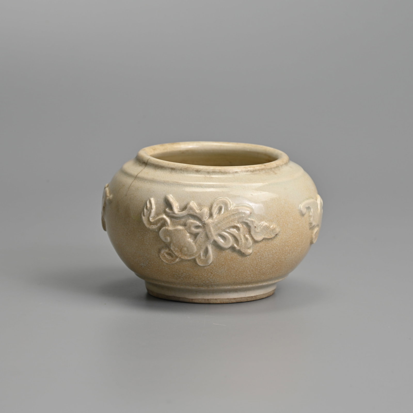 A CHINESE WHITE GLAZED PORCELAIN JAR, POSSIBLY FUJIAN DEHUA, MING DYNASTY (1368-1644).: Of squat globular from with moulded motifs to the body to include bats, a double gourd and ruyi sceptre. Covered in a an off white glaze with a fine network of crackle. 9.6cm diam.