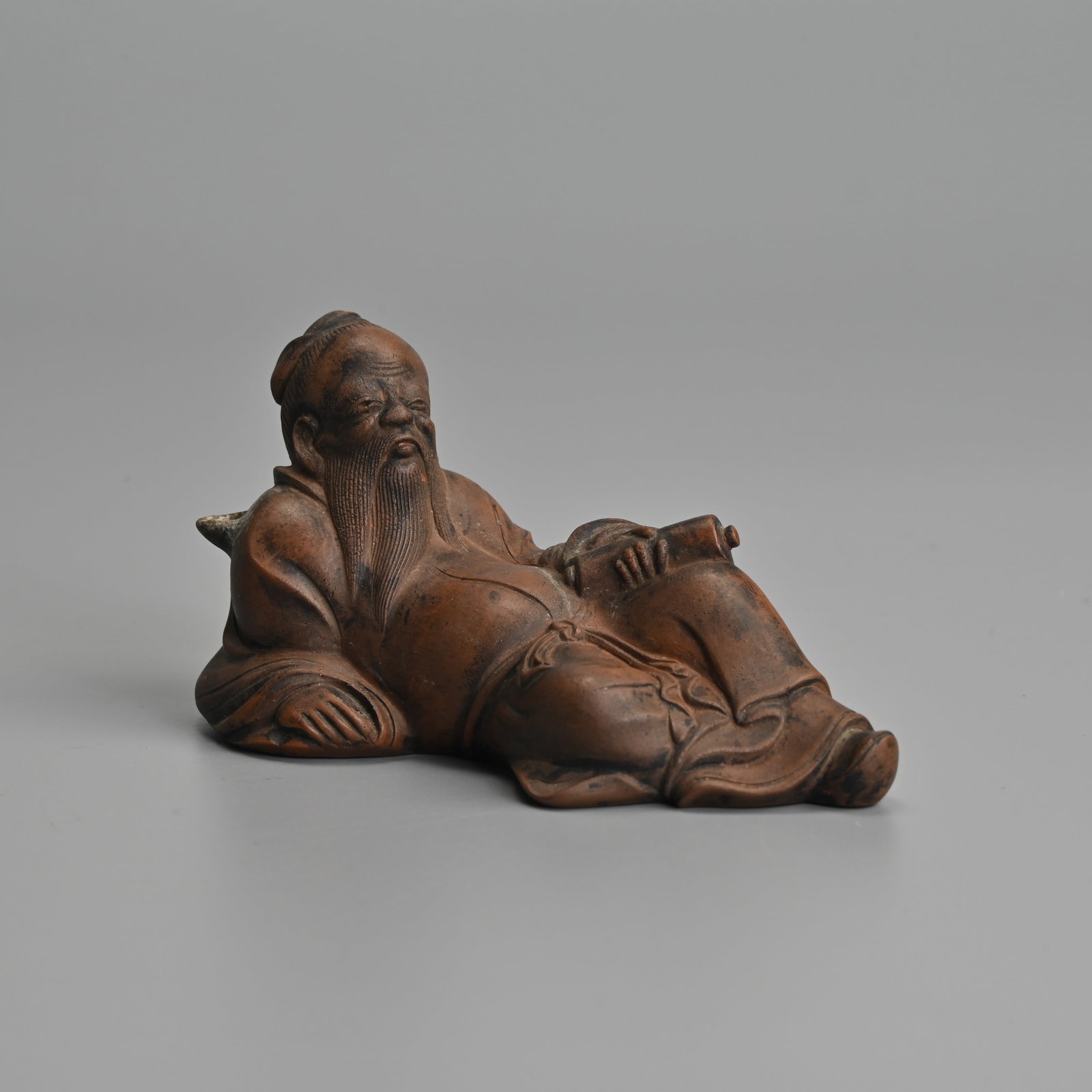 A CHINESE YIXING STONEWARE WATER DROPPER IN THE FORM OF LI BAI, QING DYNASTY.: The famous Tang dynasty poet reclining holding a scroll in his left hand. The air hole aperture behind hi left hand with shot spout at the right shoulder. 10.cm length. Provenance: Private collection,