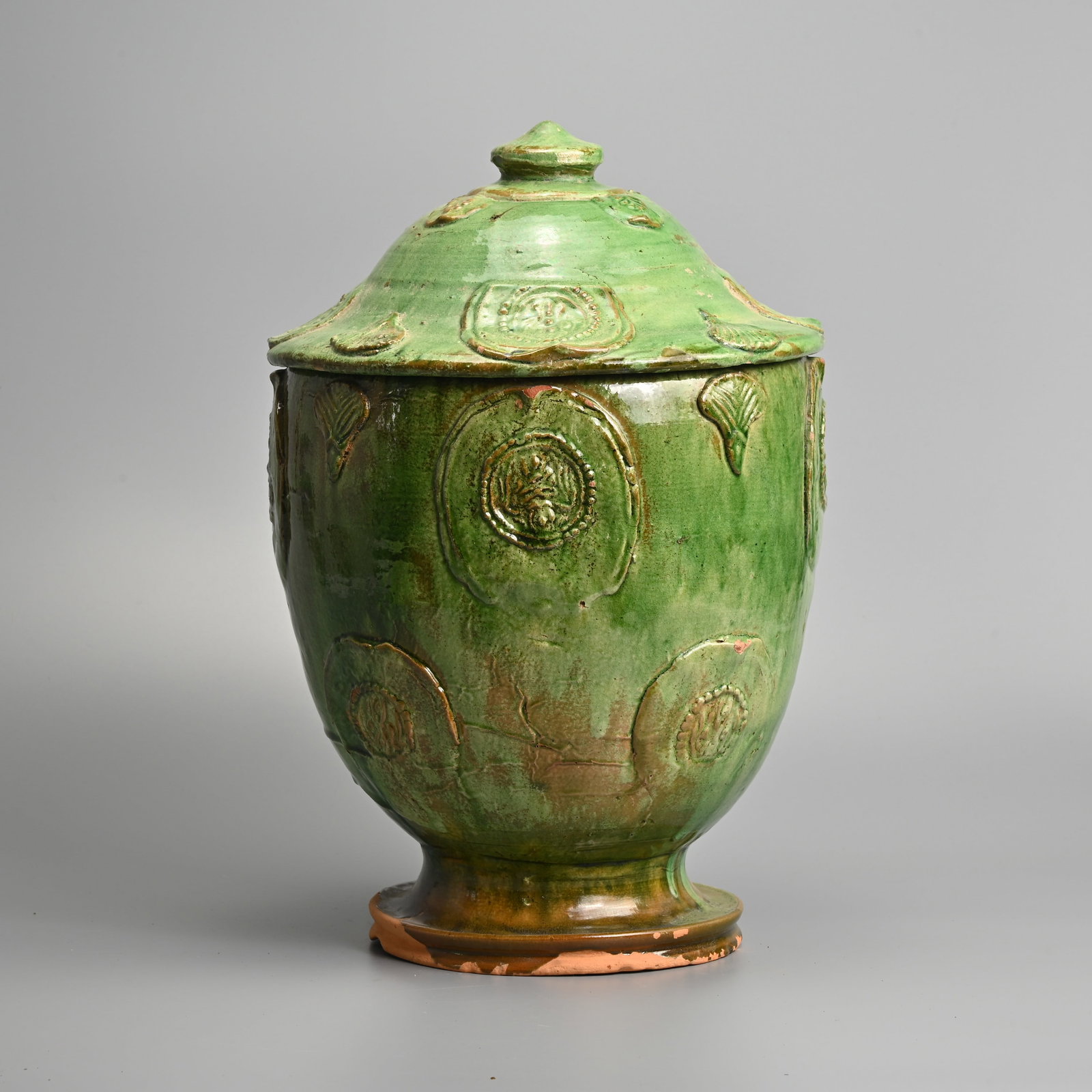 A FINE CHINESE GREEN GLAZED RED POTTERY BUDDHIST JAR, 13/14TH CENTURY.: Featuring moulded Buddhist appliqués detailing small leaves and a vajra nestled within lotus petals. Before an attractive green glaze was applied, the exterior was coated in a white slip that stops j