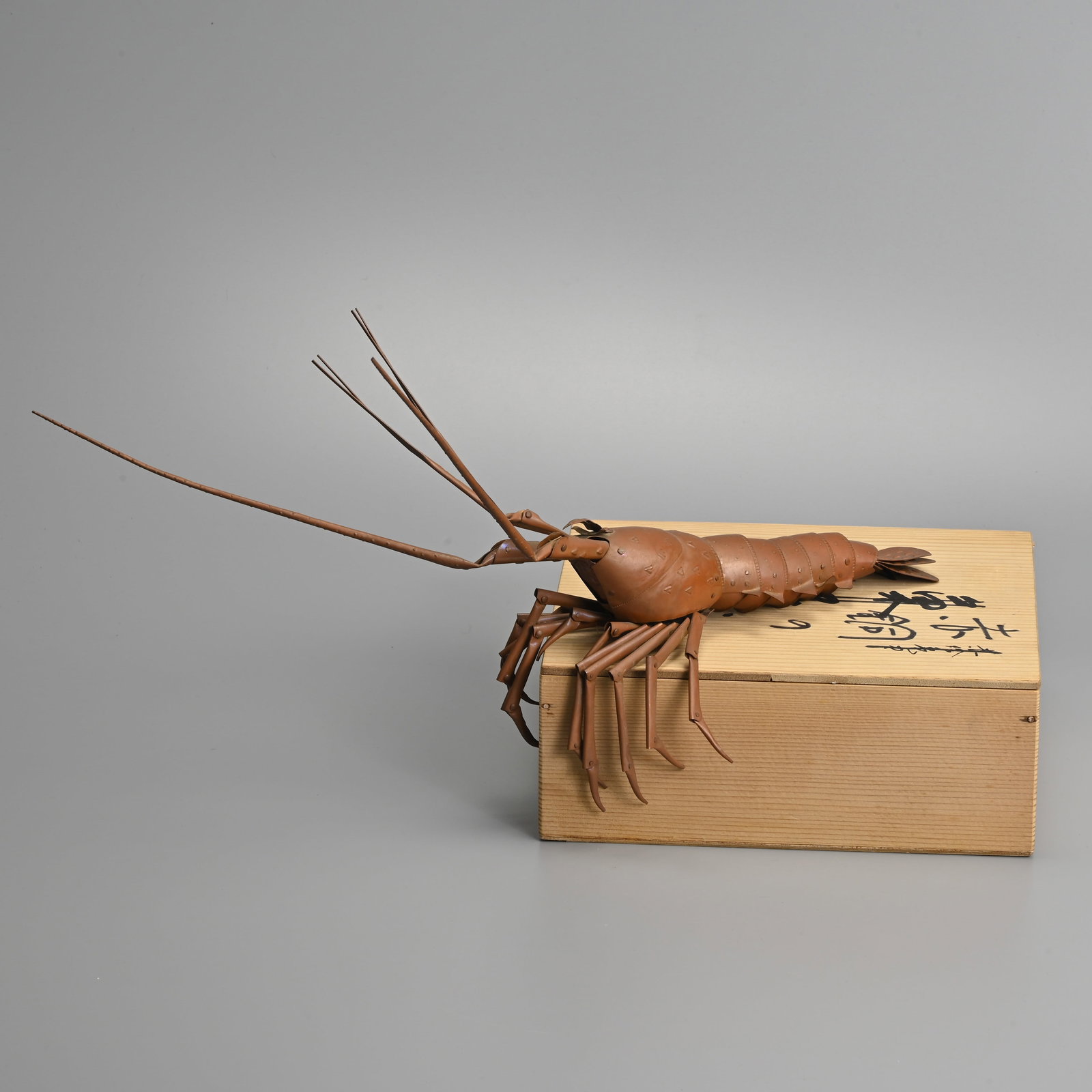 A JAPANESE COPPER JIZAI OKIMONO OF A SPINY LOBSTER, SOUYUKI MYOCHIN, 20TH CENTURY.: Signed to the underside ‘Souyuki Myochin’. Body 18.5cm (40cm total length incl. antenna), 6cm wide, weight 150g. Together with a signed tomobako wooden box. The Myôchin school was a famous lineag
