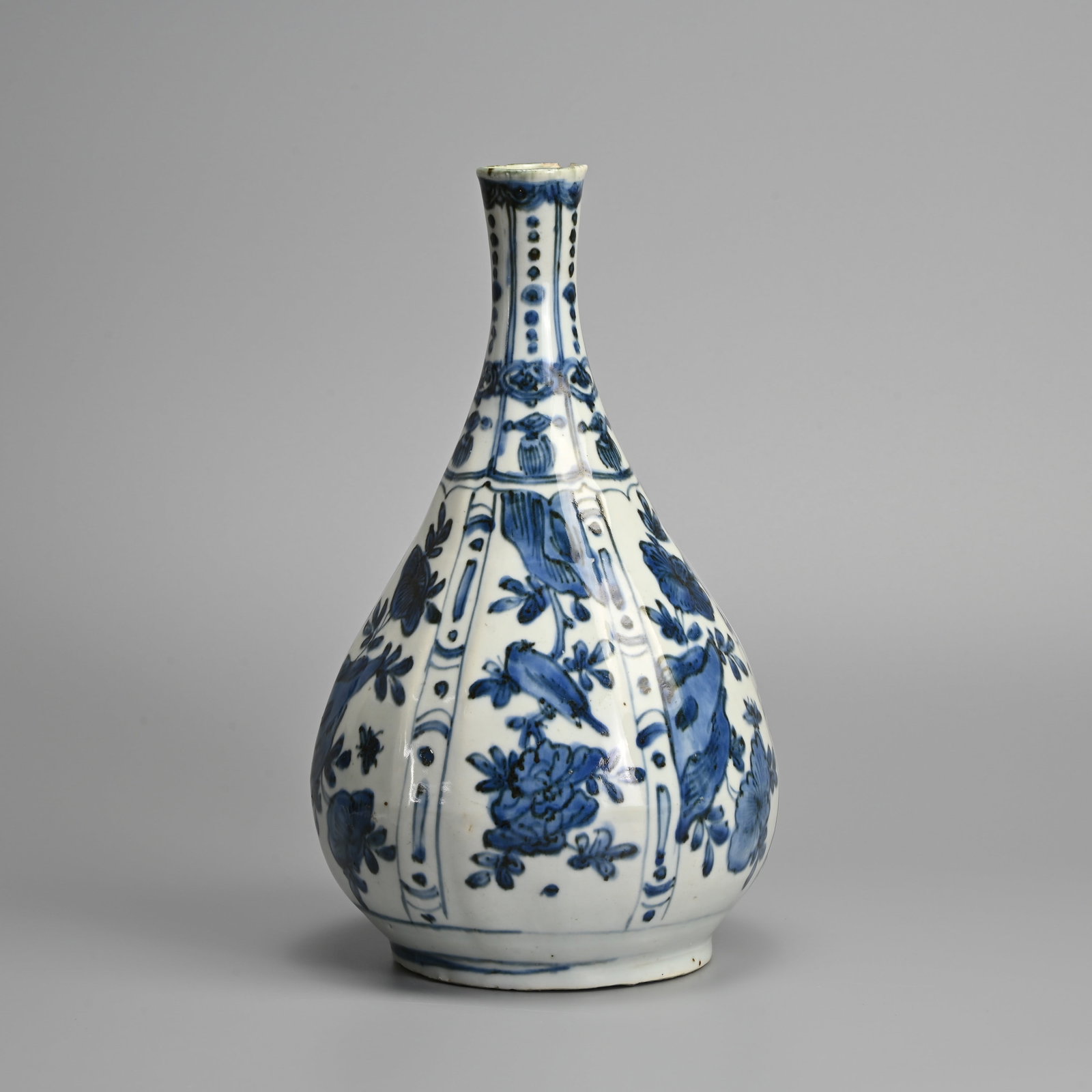 A CHINESE KRAAK BLUE AND WHITE PORCELAIN BOTTLE VASE, WANLI PERIOD (1573-1619).: A CHINESE KRAAK BLUE AND WHITE PORCELAIN BOTTLE VASE, WANLI PERIOD (1573-1619). Decorated with moulded panels enclosing birds, flowers and rockwork, all below narrow panels of beaded pendants and tass