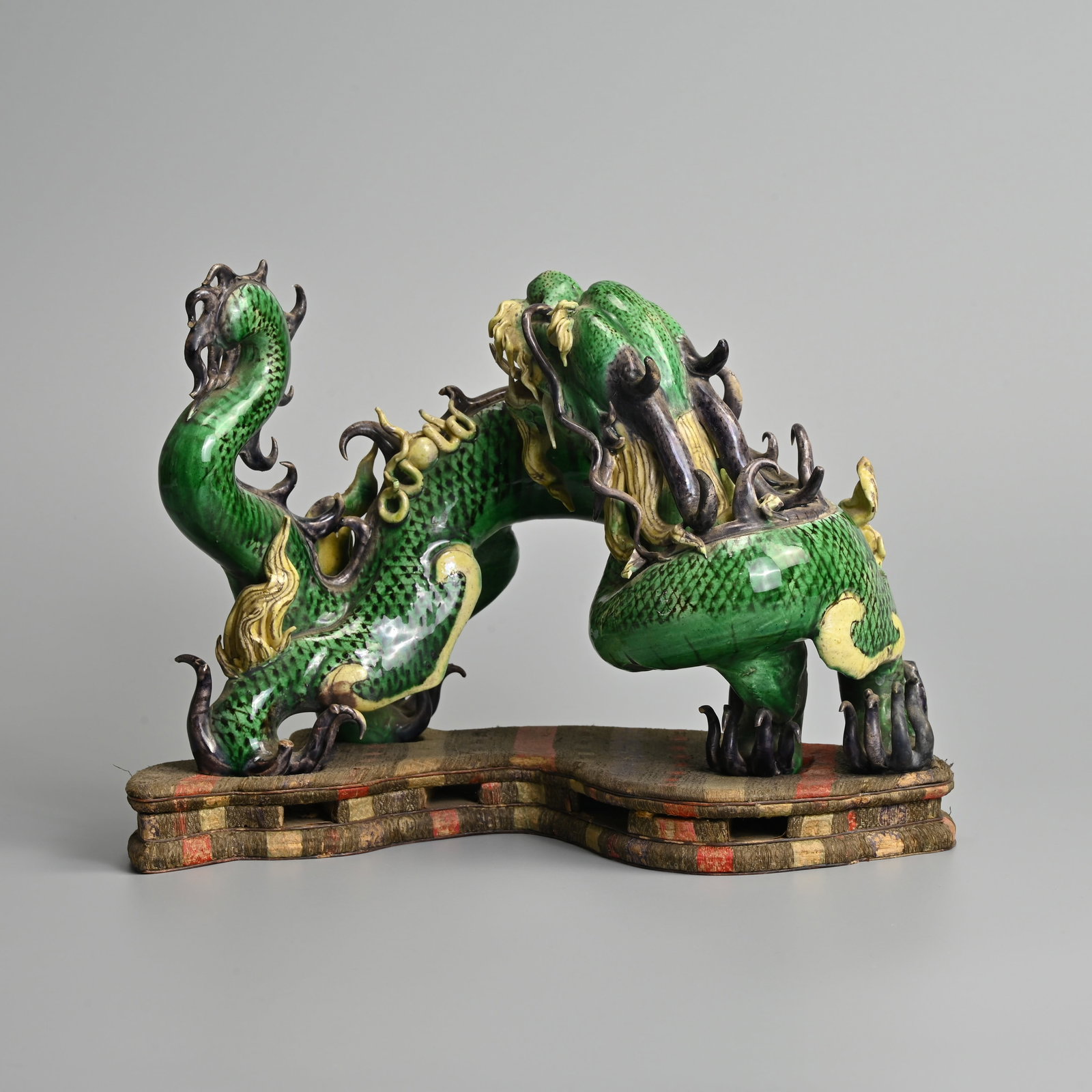 A CHINESE FAMILLE VERTE PORCELAIN MODEL OF A DRAGON WITH EMBROIDERED SILK STAND, 19TH CENTURY, QING: A CHINESE FAMILLE VERTE PORCELAIN MODEL OF A DRAGON WITH EMBROIDERED SILK STAND, 19TH CENTURY, QING DYNASTY. Well modelled dragon standing on four legs with its head turned towards its back, with Its 