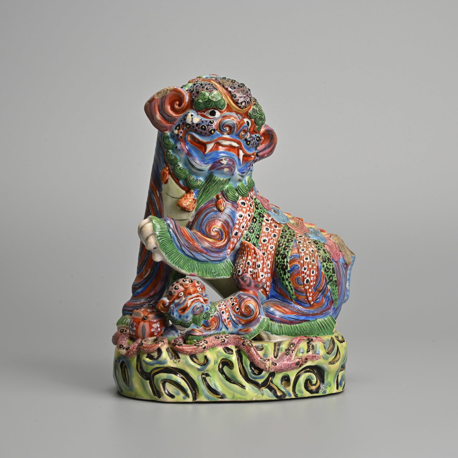 A CHINESE POLYCHROME ENAMELLED PORCELAIN FIGURE OF A BUDDHIST LION, 19TH CENTURY.: A CHINESE POLYCHROME ENAMELLED PORCELAIN FIGURE OF A BUDDHIST LION, 19TH CENTURY. The lion seated with its paw raised with its cub and ribboned ball. Colourfully enamelled throughout. 21cm tall.