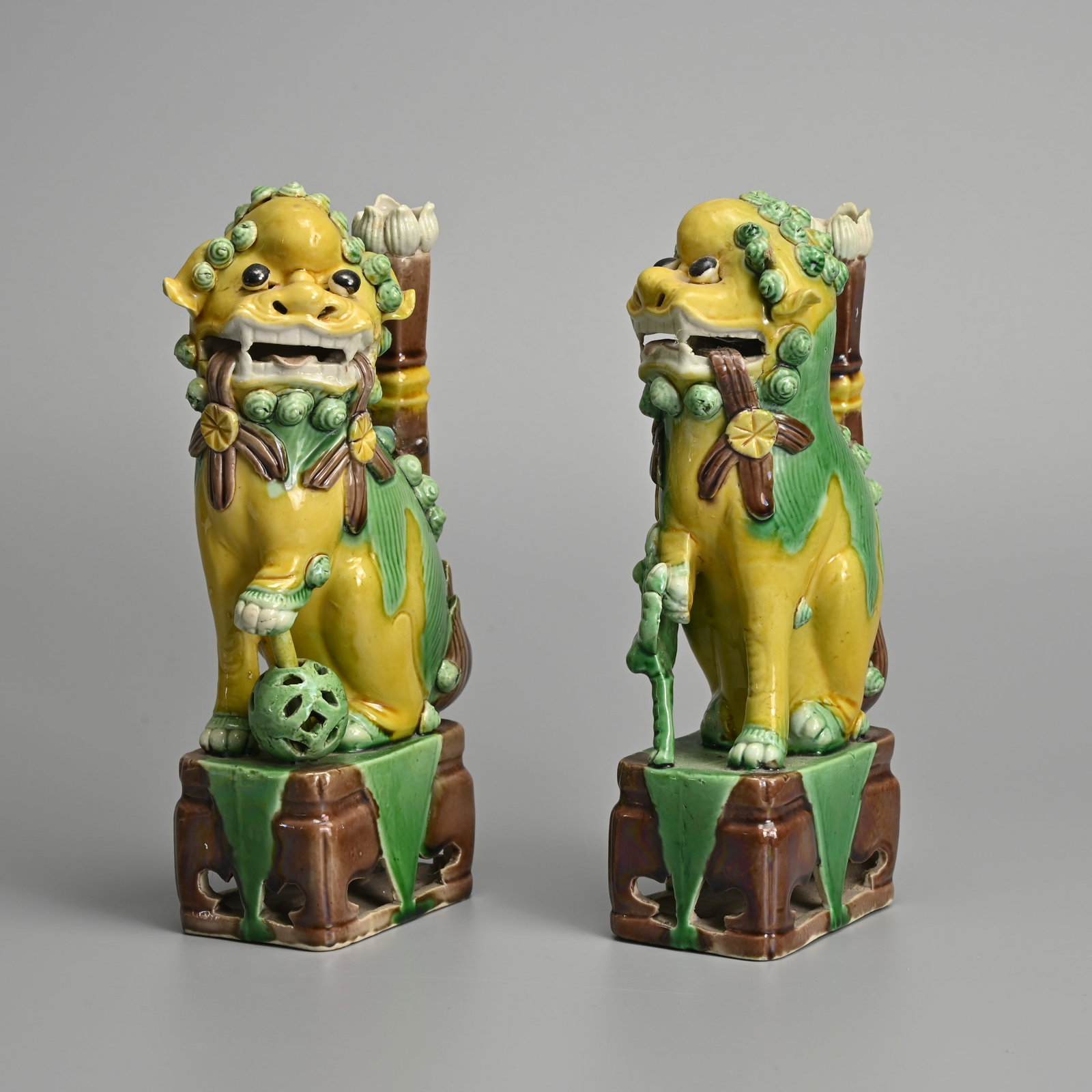 A PAIR OF CHINESE GREEN, YELLOW AND AUBERGINE GLAZED PORCELAIN 'LION' JOSS STICK HOLDERS, 19/20TH: A PAIR OF CHINESE GREEN, YELLOW AND AUBERGINE GLAZED PORCELAIN 'LION' JOSS STICK HOLDERS, 19/20TH CENTURY. The lions seated, one with a cub and the other with its paw on a pierced ball. Each with flow