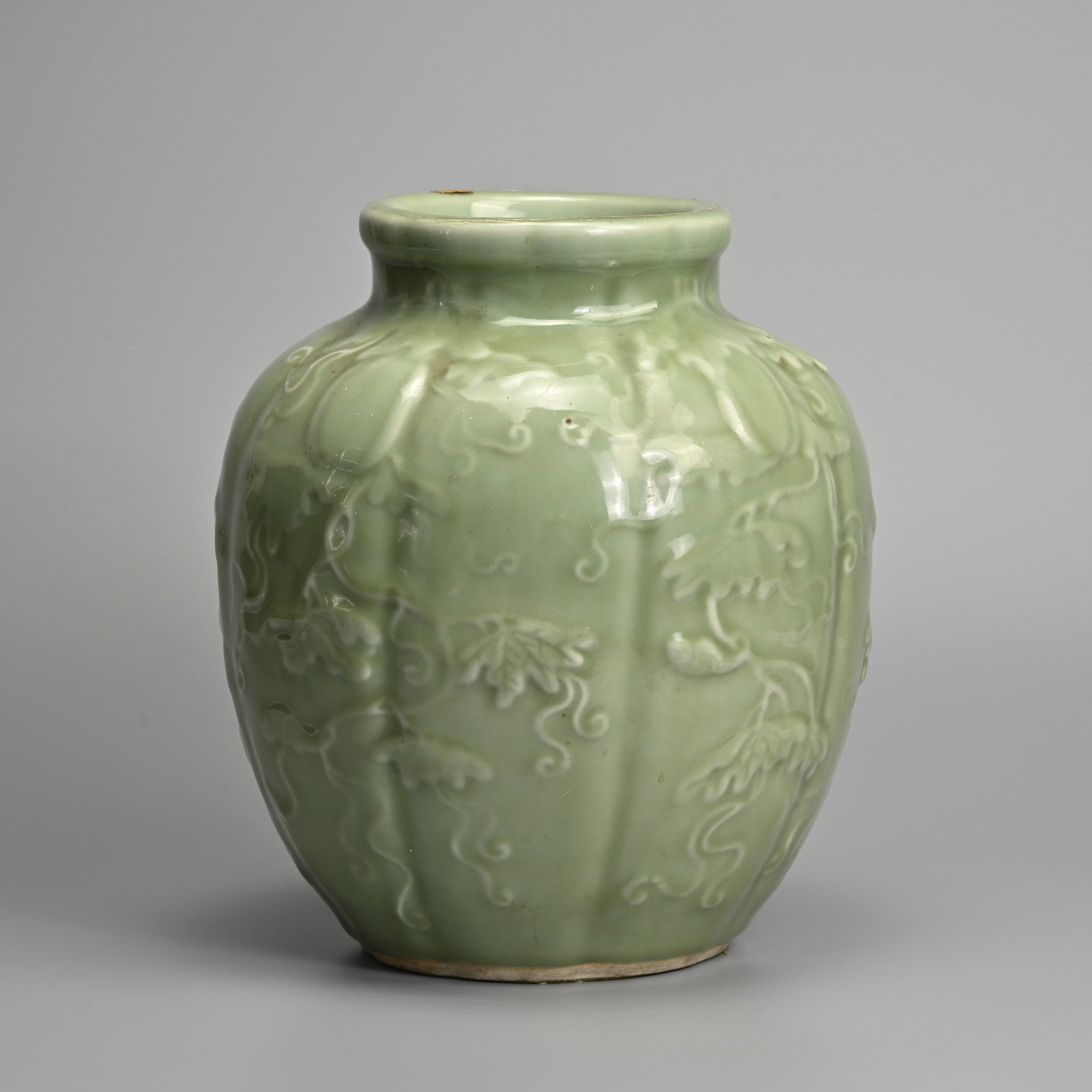 A CHINESE MOULDED OCTAGONAL LOBED CELADON GLAZED PORCELAIN JAR, 19TH CENTURY.: A CHINESE MOULDED OCTAGONAL LOBED CELADON GLAZED PORCELAIN JAR, 19TH CENTURY. Heavily potted, decorated with melon vines, butterfly and peony blooms. 25cm tall.