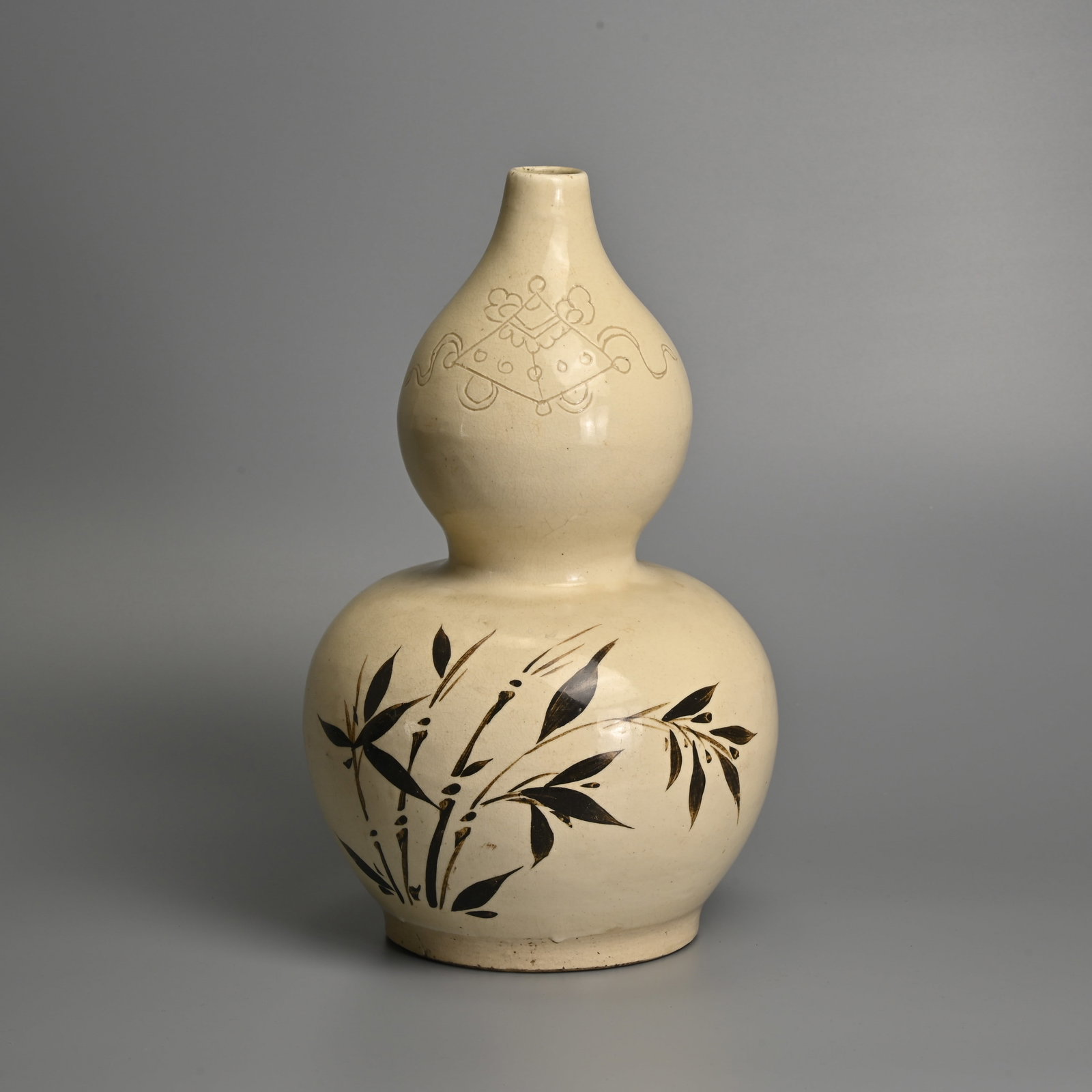 A CHINESE CIZHOU TYPE BROWN SLIP DECORATED DOUBLE GOURD VASE.: A CHINESE CIZHOU TYPE BROWN SLIP DECORATED DOUBLE GOURD VASE. Covered in a cream coloured glaze and decorated in brown slip with bamboo and inscription. An incised kite motif to the neck. 34cm tall.