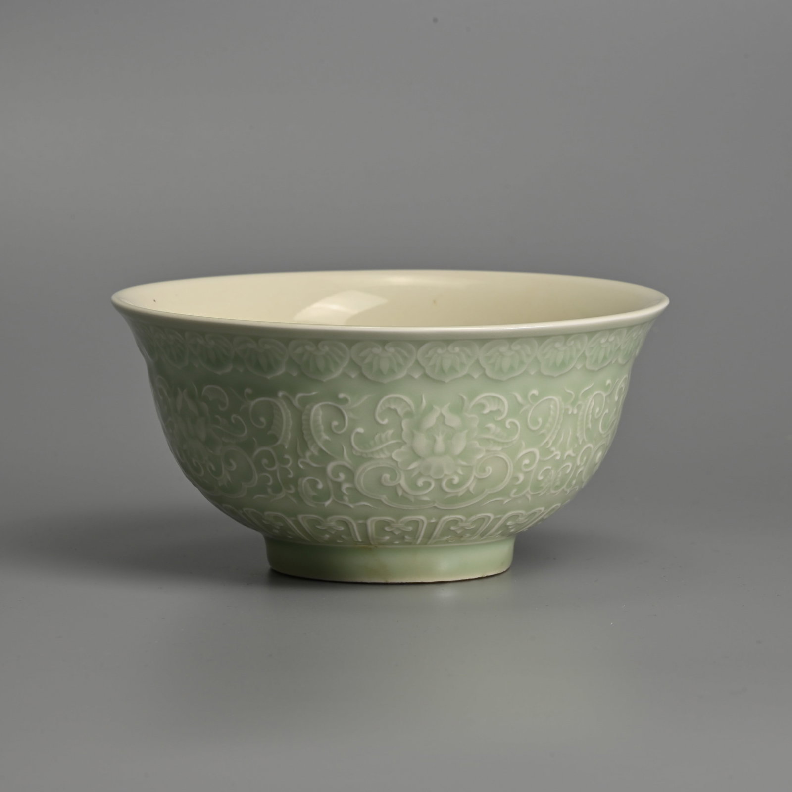 A CHINESE CELADON GLAZED PORCELAIN BOWL.: A CHINESE CELADON GLAZED PORCELAIN BOWL. Crisply moulded with lotus scrolls between lappets and ruyi covered in a pale celadon glaze. The interior covered in a white glaze. 15.8cm diam.