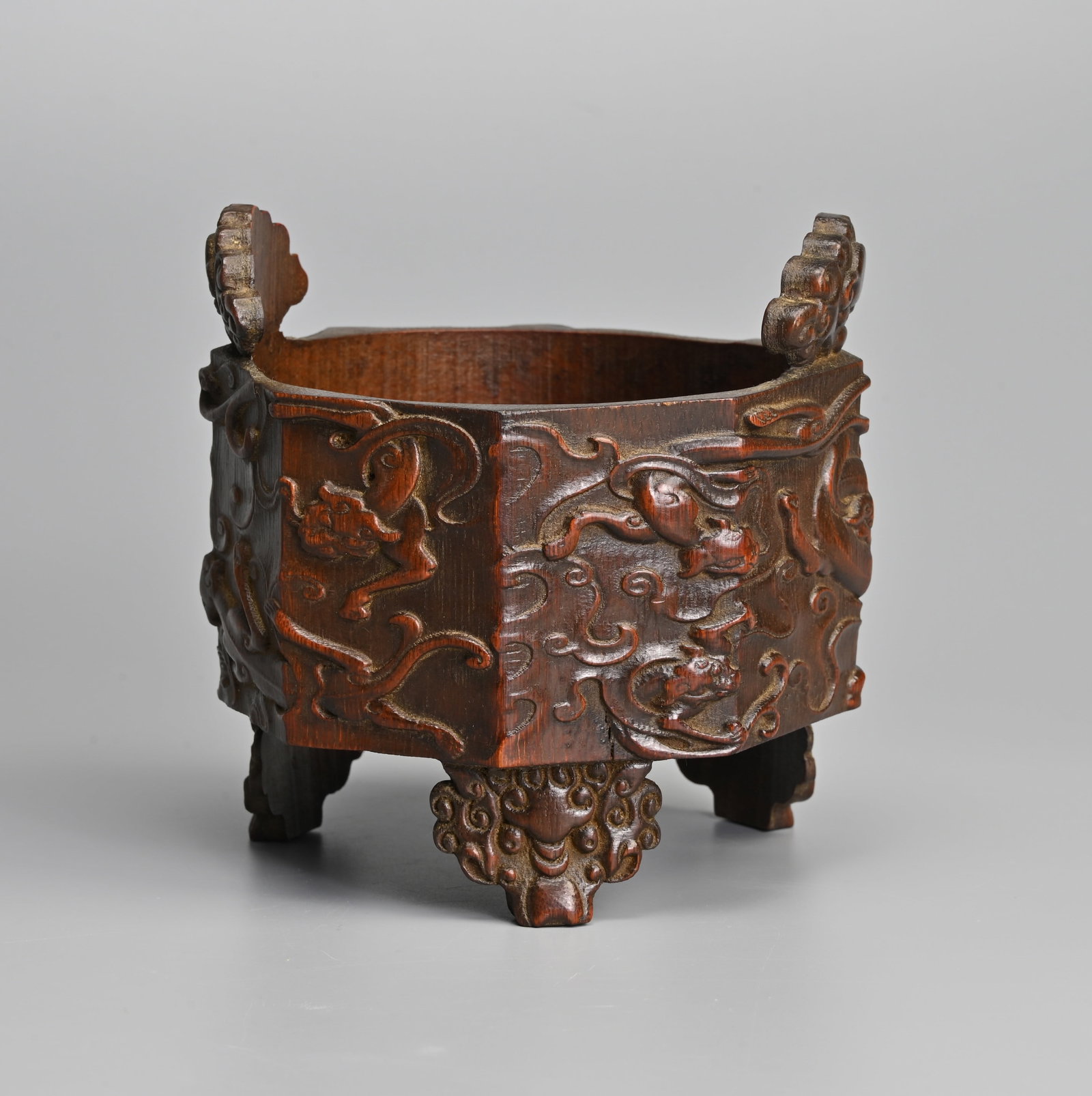 A CHINESE CARVED BAMBOO 'NINE CHILONG' TRIPOD CENSER, QING DYNASTY.: A CHINESE CARVED BAMBOO 'NINE CHILONG' TRIPOD CENSER, QING DYNASTY. Of octagonal form carved in relief with nine chilong, with lion form feet and handles. 13cm tall including handles x 13cm wide.