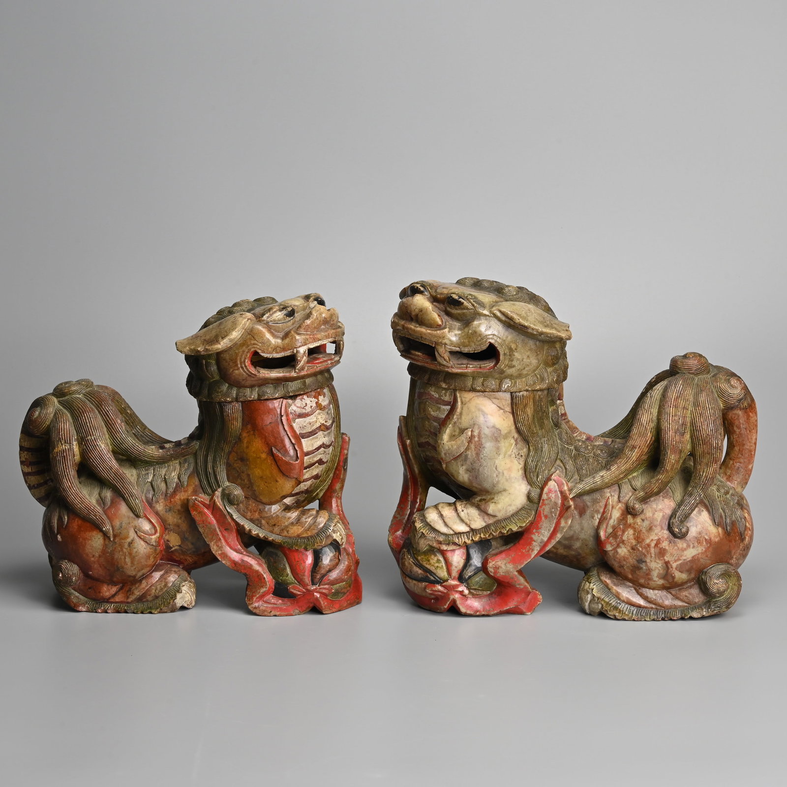 A LARGE PAIR OF CHINESE CARVED SOAPSTONE 'MALE FOO DOG' CENSERS, SOUTH CHINA, 19TH CENTURY.: A LARGE PAIR OF CHINESE CARVED SOAPSTONE 'MALE FOO DOG' CENSERS, SOUTH CHINA, 19TH CENTURY. Separately carved heads with metal ring liners in the body. Areas picked out in red lacquer. The larger lion