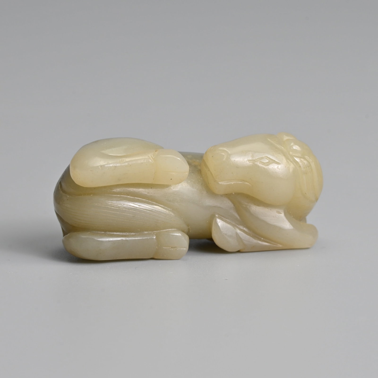 A CHINESE CARVED CELADON JADE FIGURE OF A RECUMBENT HORSE, MING / QING DYNASTY.: A CHINESE CARVED CELADON JADE FIGURE OF A RECUMBENT HORSE, MING / QING DYNASTY. Well carved, with its front legs turned over to its side with its head turned. 5cm length.