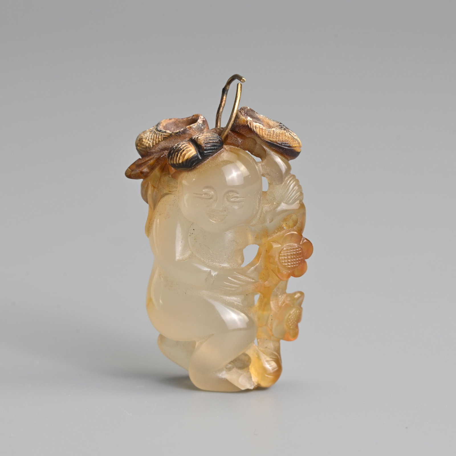 A FINE CHINESE CARVED AGATE 'BOY' PENDANT, 18/19TH CENTURY.: A FINE CHINESE CARVED AGATE 'BOY' PENDANT, 18/19TH CENTURY. The boy holding onto a floral stem with a pair of russet brown shoes. 4,5cm length.