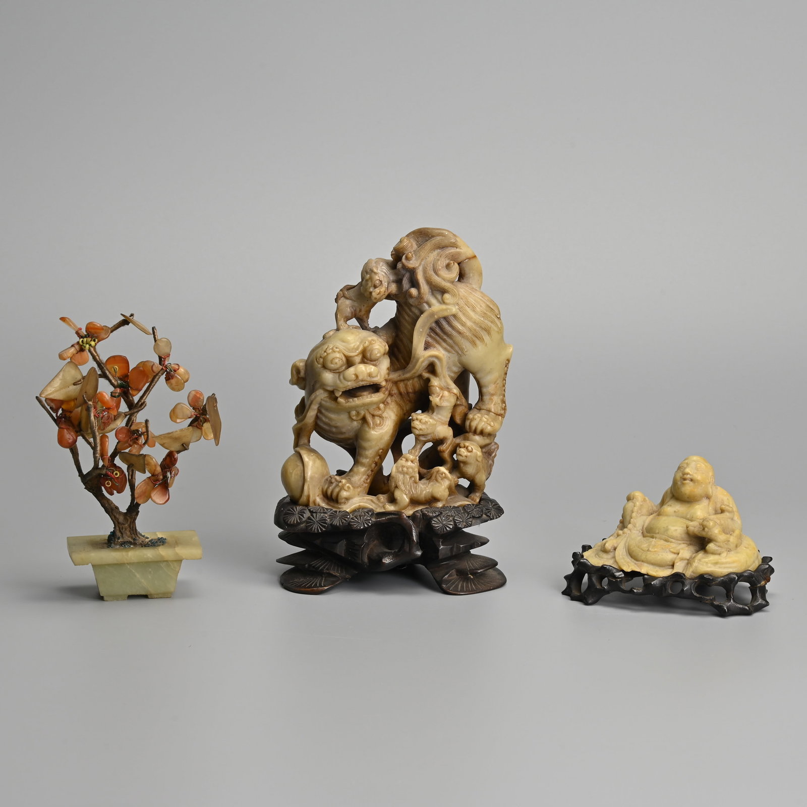 A CHINESE CARVED SOAPSTONE GUARDIAN LION GROUP TOGETHER WITH A FIGURE OF BUDAI AND A STONE BONSAI (1 of 15)