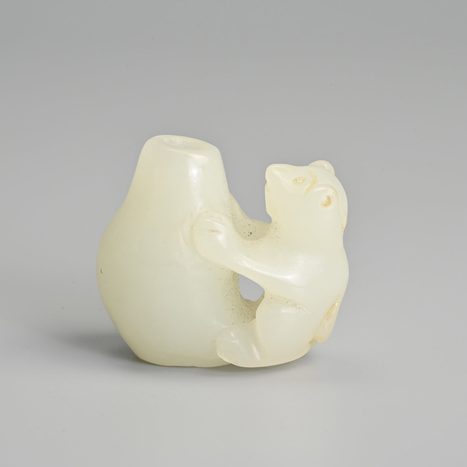 A CHINESE CARVED WHITE JADE BEAR AND POT.: A CHINESE CARVED WHITE JADE BEAR AND POT. The bear seated with its paws against the pot, with a hollowed section to the inside of the pot. 4cm x 5cm.