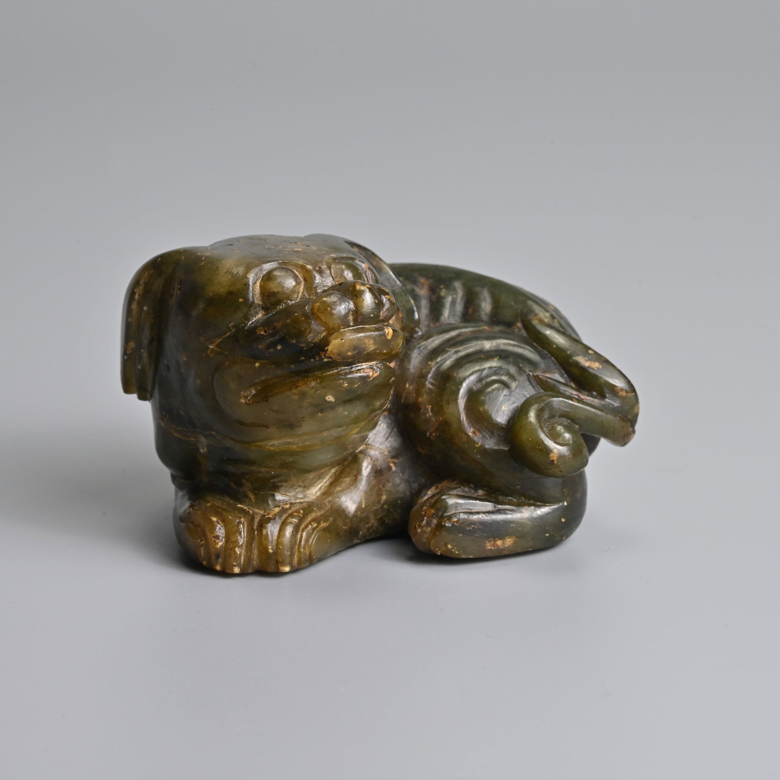 A CHINESE CARVED GREEN JADE FIGURE OF A RECUMBENT MYTHICAL BEAST.: A CHINESE CARVED GREEN JADE FIGURE OF A RECUMBENT MYTHICAL BEAST. The figure curled with its head raised. 7.5cm length x 4.6cm tall.