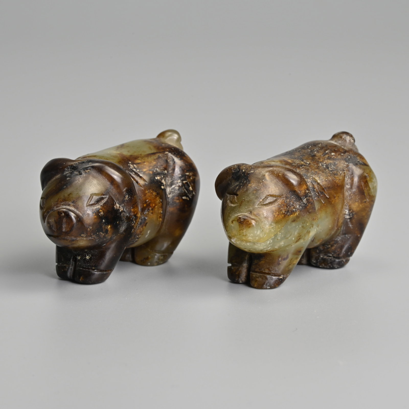 A PAIR OF CHINESE GREEN AND DARK BROWN JADE FIGURES OF PIGS. (1 of 9)