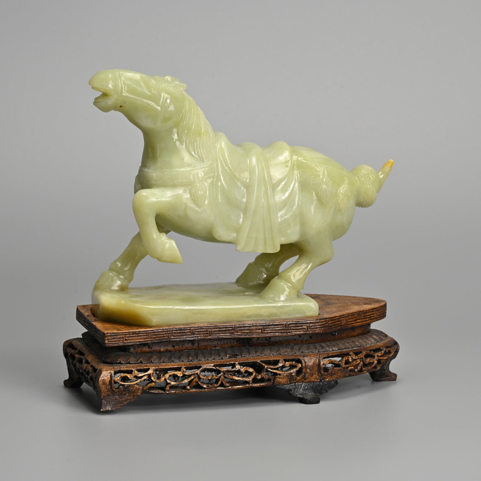 A CHINESE PALE GREEN JADE FIGURE OF A CAPARISONED HORSE WITH WOODEN STAND, 20TH CENTURY. (1 of 9)