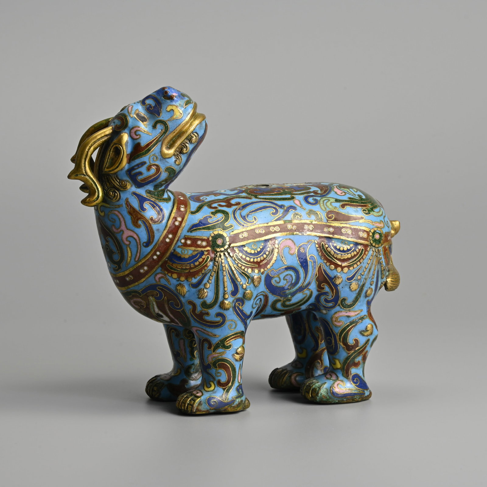 A CHINESE CLOISONNE ENAMEL AND GILT DECORATED FIGURE OF A MYTHICAL BEAST, 19/20TH CENTURY.: A CHINESE CLOISONNE ENAMEL AND GILT DECORATED FIGURE OF A MYTHICAL BEAST, 19/20TH CENTURY. Standing foursquare with its head turned towards its back. 17cm length x 15cm tall.