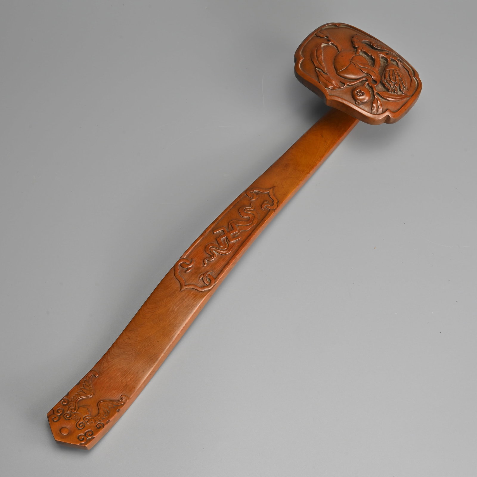 A CHINESE CARVED HUANGYANG RUYI SCEPTRE, QIANLONG MARK.: A CHINESE CARVED HUANGYANG RUYI SCEPTRE, QIANLONG MARK. The curved handle in low relief featuring a Buddhist swastika and cloud within a ruyi-shaped border, the end of the handle with a bat. The head 