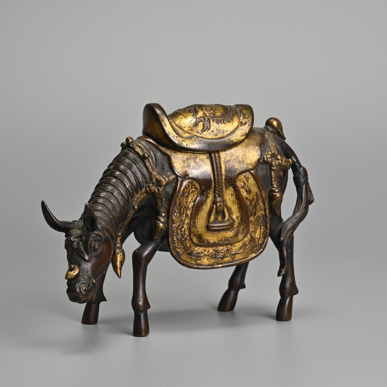A CHINESE PARCEL GILT BRONZE 'MULE' CENSER, 19TH CENTURY.: A CHINESE PARCEL GILT BRONZE 'MULE' CENSER, 19TH CENTURY. Standing with its head lowered wearing a gilt decorated saddle. The separately cast saddle cover decorated in relief with dragon. 19cm length.