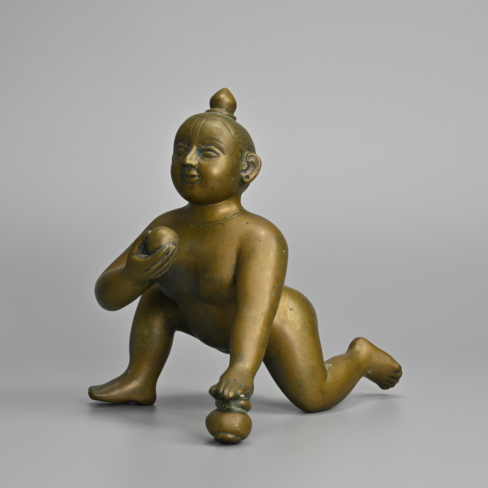 AN INDIAN BRONZE FIGURE OF KRISHNA 'BUTTER THIEF', EARLY 20TH CENTURY.: AN INDIAN BRONZE FIGURE OF KRISHNA 'BUTTER THIEF', EARLY 20TH CENTURY. Heavily cast figure depicted as an infant crawling with his right hand raised holding a ball of butter and his left hand on a pot
