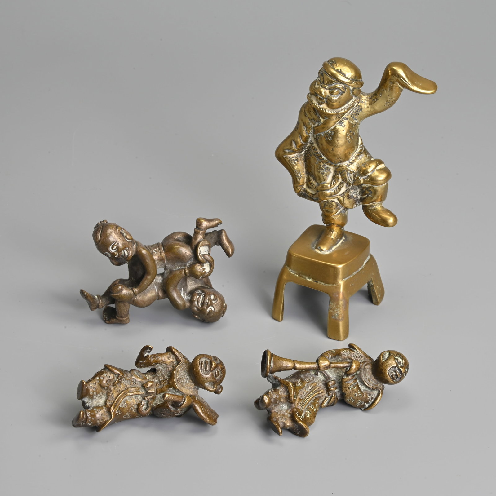 A GROUP OF CHINESE BRASS BRONZE FIGURES AND PAPERWEIGHT, 19/20TH CENTURY.: A GROUP OF CHINESE BRASS BRONZE FIGURES AND PAPERWEIGHT, 19/20TH CENTURY. To include a man standing on one leg on raised base; A 'Hehe Erxian' paper weight; Together with a pair of figures. 7cm - 12.5