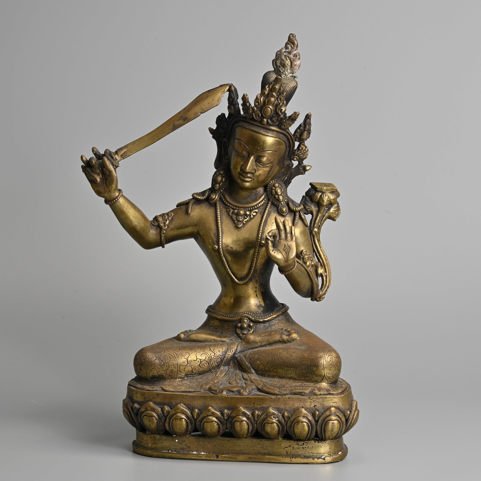 A TIBETAN BRASS FIGURE OF MANJUSHRI, 20TH CENTURY.: A TIBETAN BRASS FIGURE OF MANJUSHRI, 20TH CENTURY. Seated on a lotus base holding the sword of wisdom with a lotus spray to the left shoulder supporting the Prajnaparamita sutra text. 32.5cm tall.