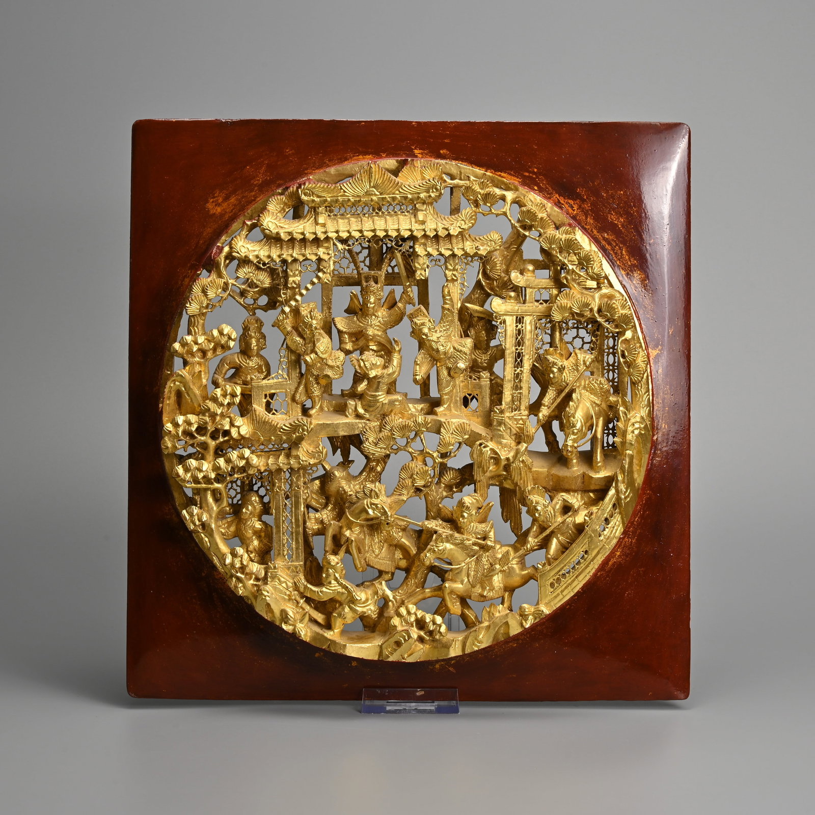 A CHINESE GILT RED LACQUER WOOD CIRCULAR PANEL, 19/20TH CENTURY.: A CHINESE GILT RED LACQUER WOOD CIRCULAR PANEL, 19/20TH CENTURY. Carved and pierced in deep relief depicting a 'battle scene' with figures on horse back within a pagoda setting with pine trees, mounte