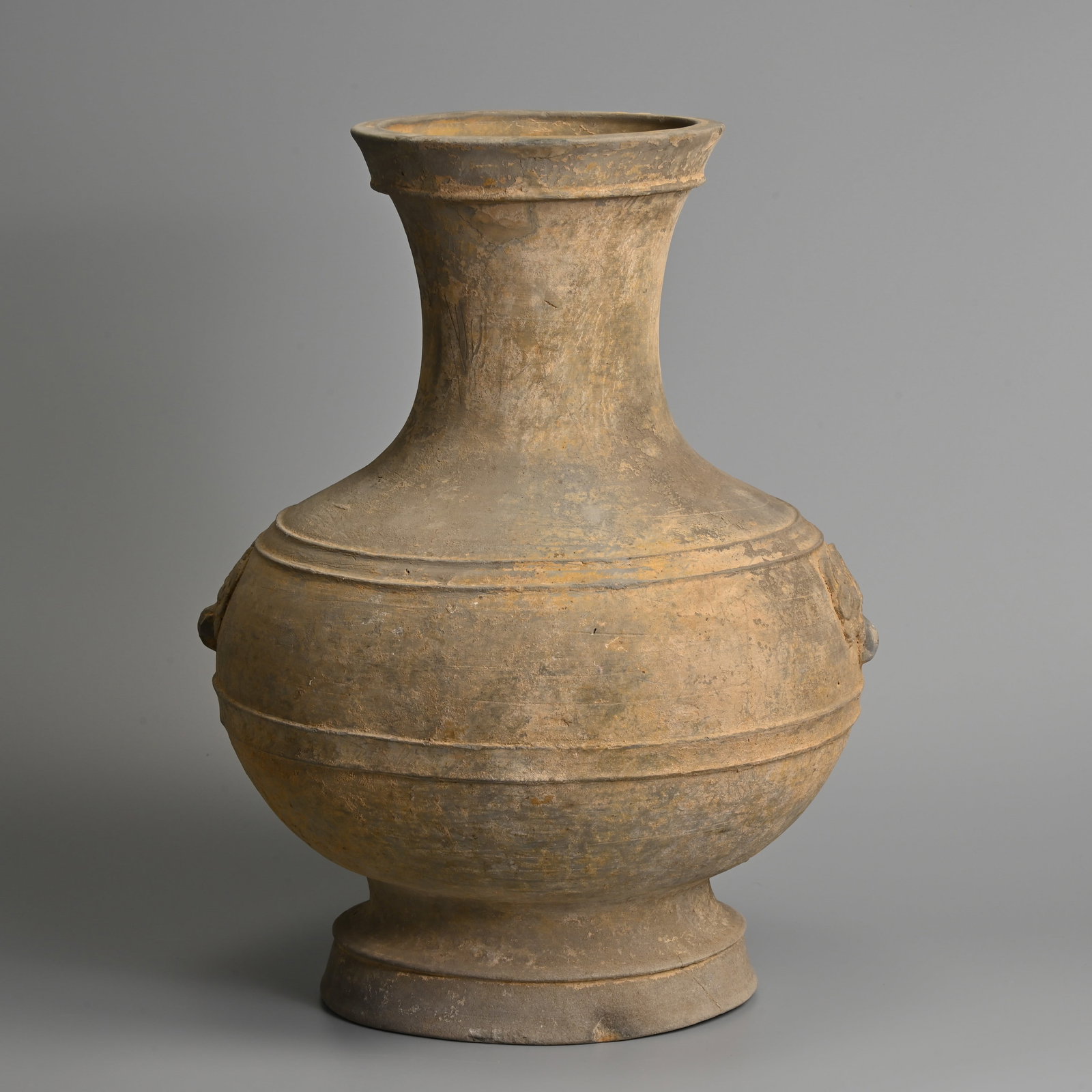 A LARGE CHINESE GREY POTTERY HU JAR, HAN DYNASTY (206BC - 220AD).: A LARGE CHINESE GREY POTTERY HU JAR, HAN DYNASTY (206BC - 220AD). With taotie mask handles, decorated with horizontal linear bands. 41cm tall. Provenance: Private English collection acquired in Hong K