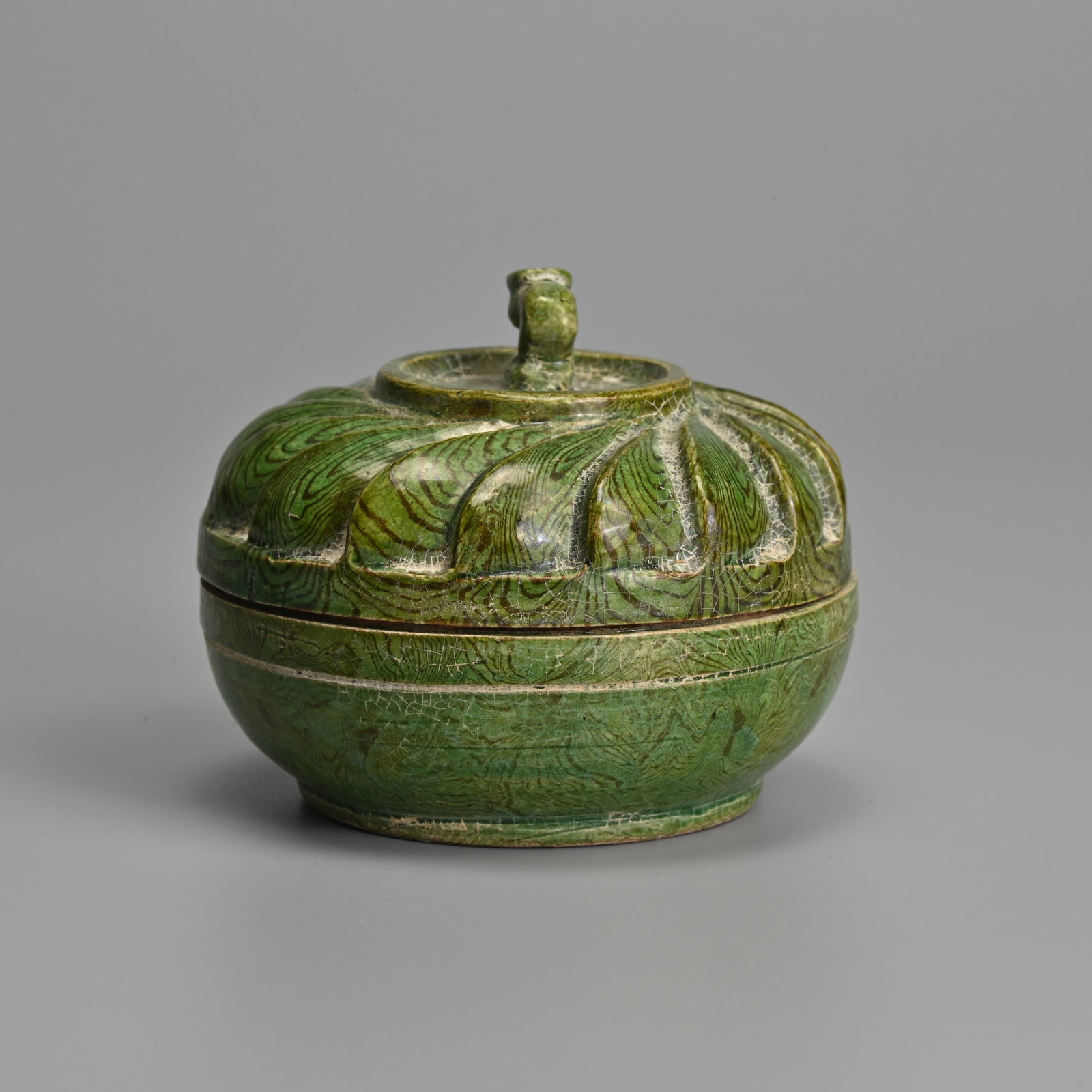 A CHINESE MARBLED GREEN GLAZED BOX AND COVER, SONG - MING DYNASTY.: A CHINESE MARBLED GREEN GLAZED BOX AND COVER, SONG - MING DYNASTY. Or circular form with overlapped carved cover and finial covered in a green glaze with brown marbling within the buff body, the rim o